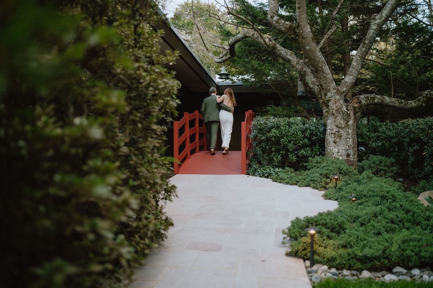 View of couple entering red doorway through lush garden pathway.