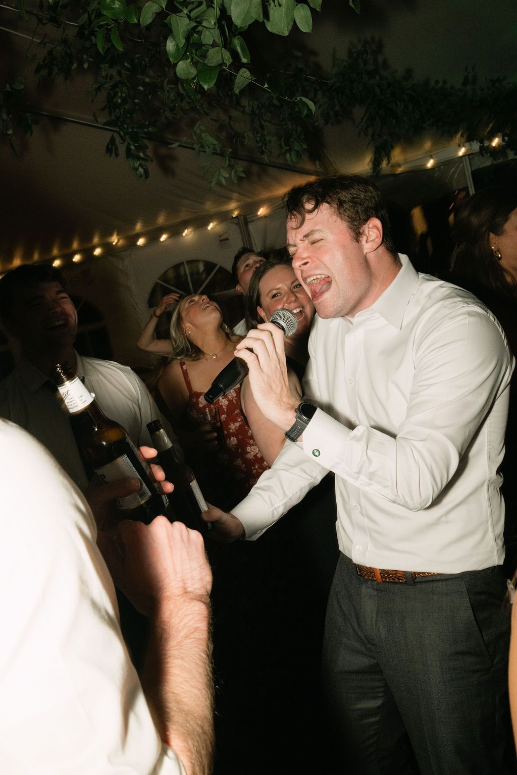 Guests in formal attire dance and celebrate energetically under decorative string lights.