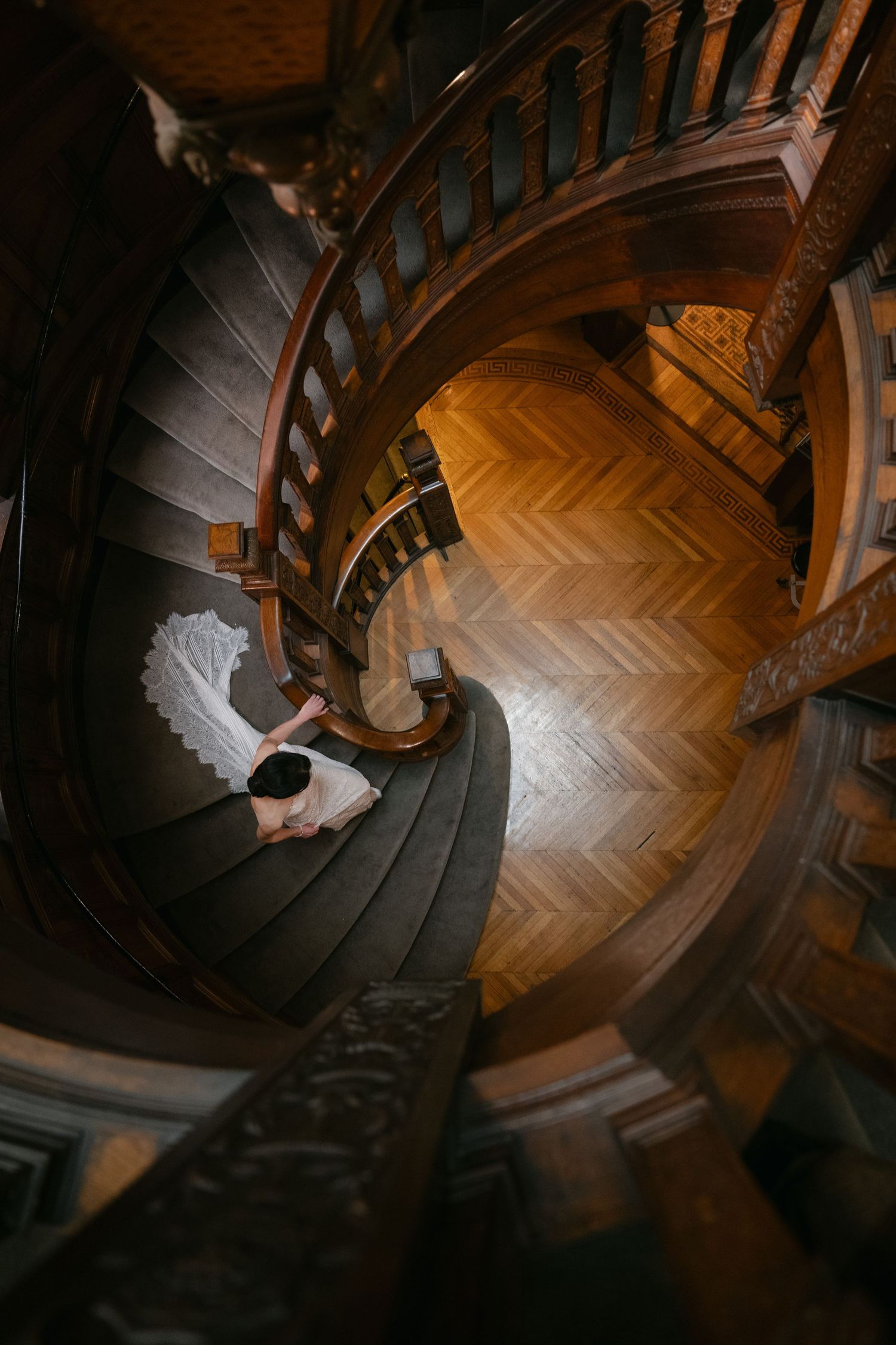 Aerial view of a spiral staircase with a wedding dress train flowing down the wooden steps.