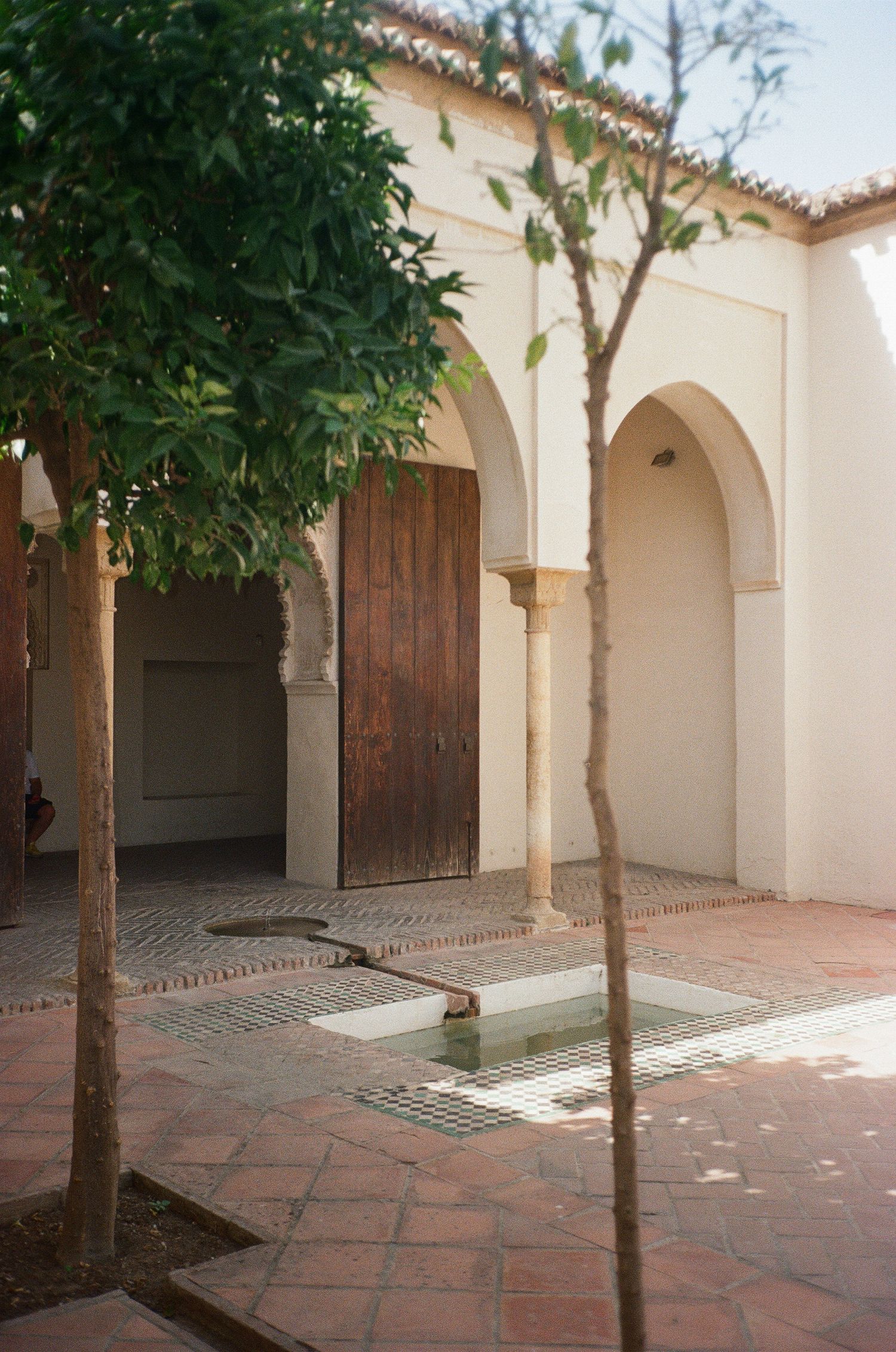 Mediterranean courtyard with arched colonnade, wooden doors, and potted trees creating a peaceful atmosphere.