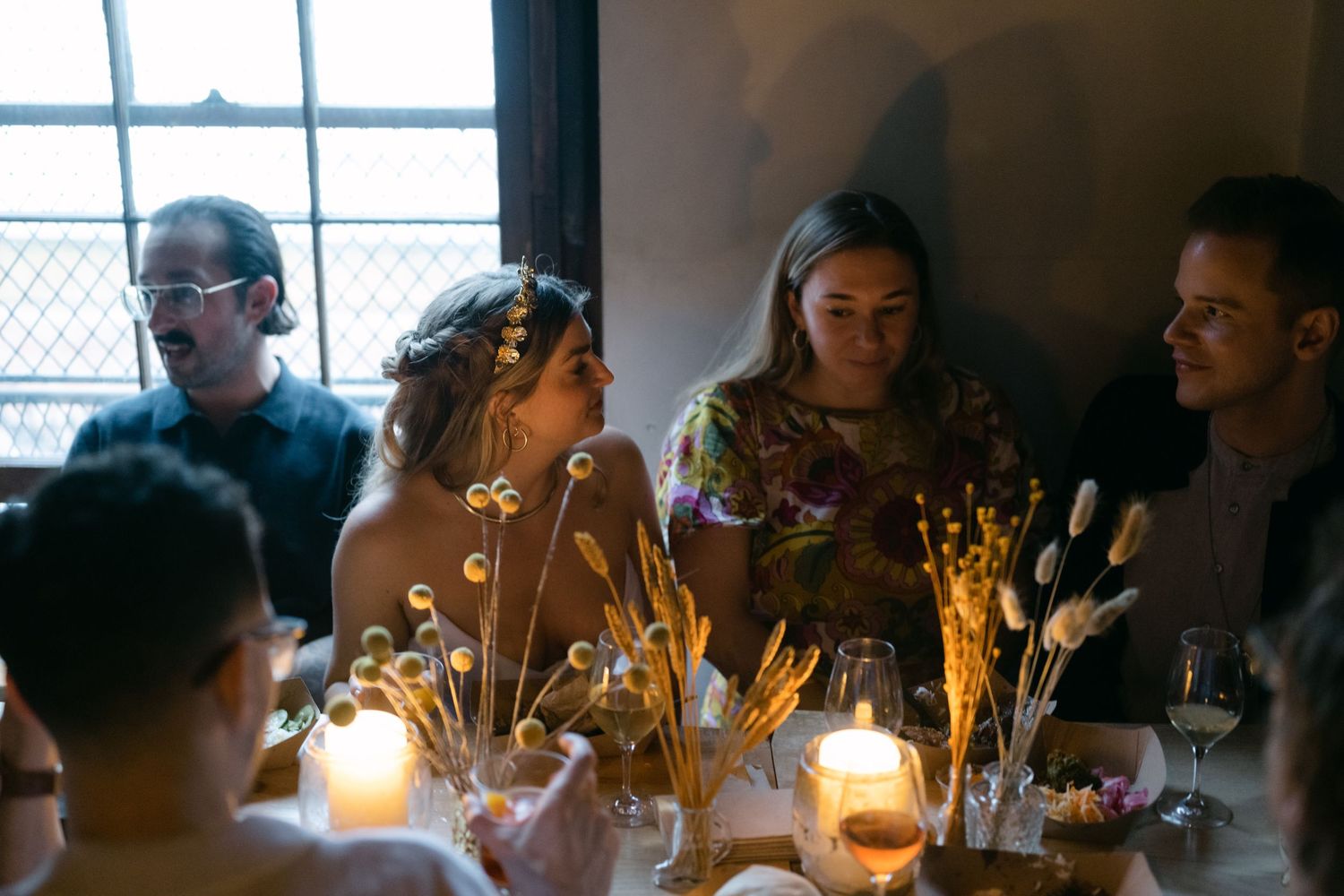 Warm candlelit dinner scene with guests gathered around a table with glowing string lights.