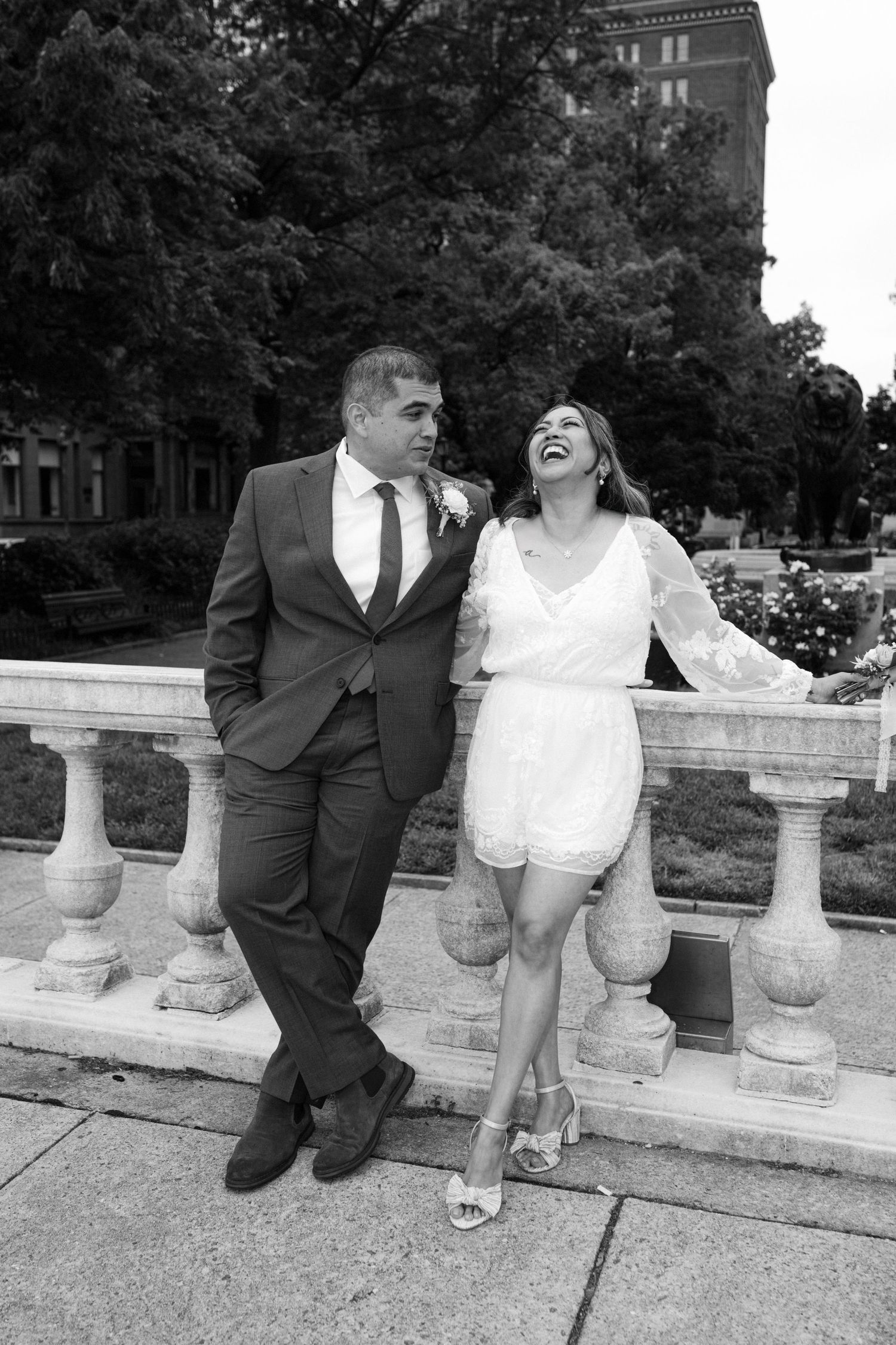 A couple sharing a candid laughing moment together on a stone balcony in black and white photography.