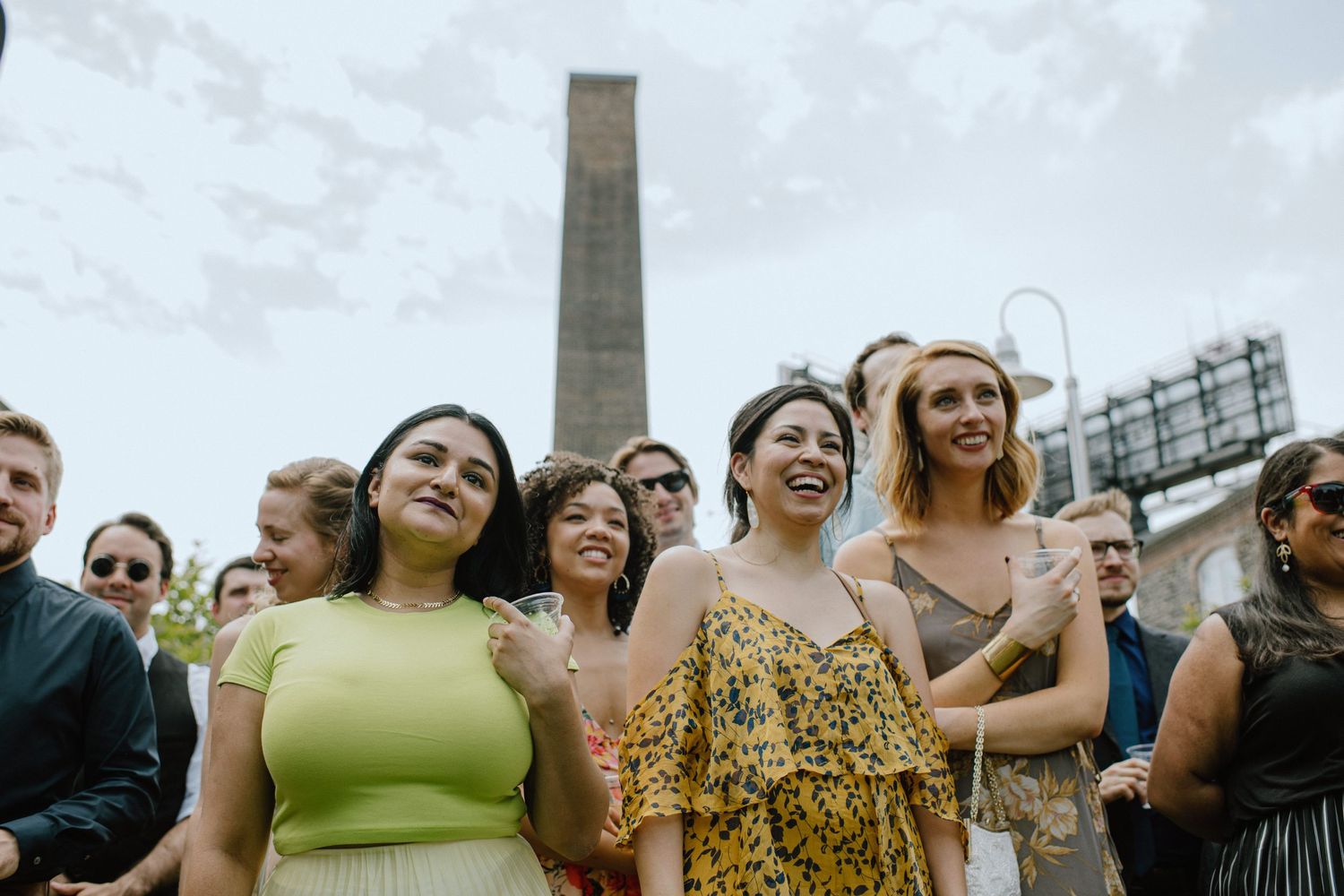 Group of wedding guests laughing together with industrial chimney in background.