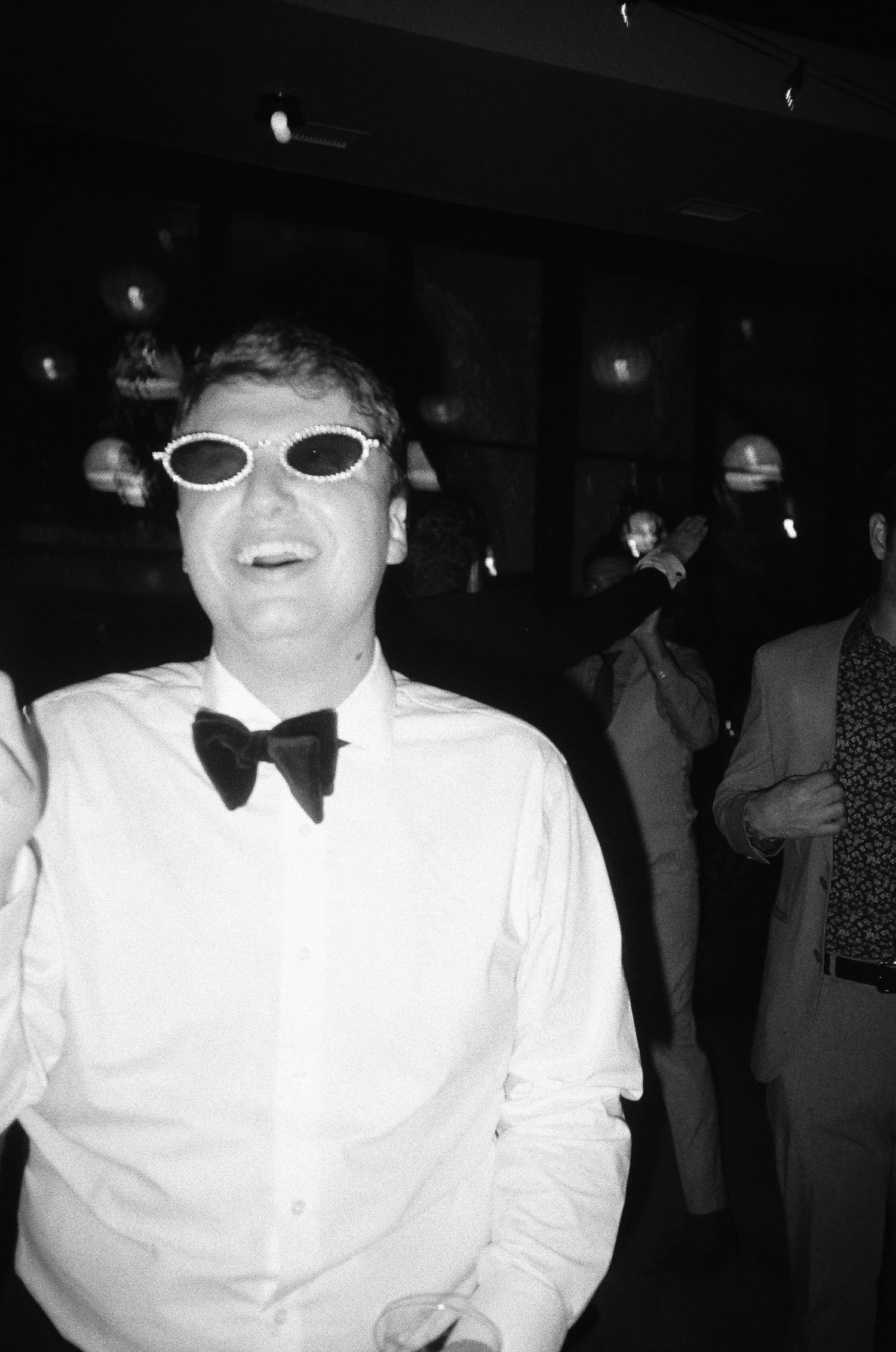 Person wearing sunglasses and a bow tie smiling at a formal event.