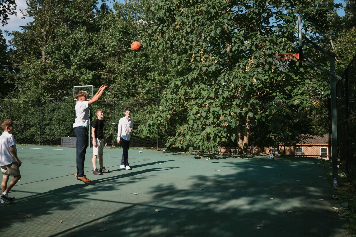 People playing basketball on an outdoor court surrounded by trees.
