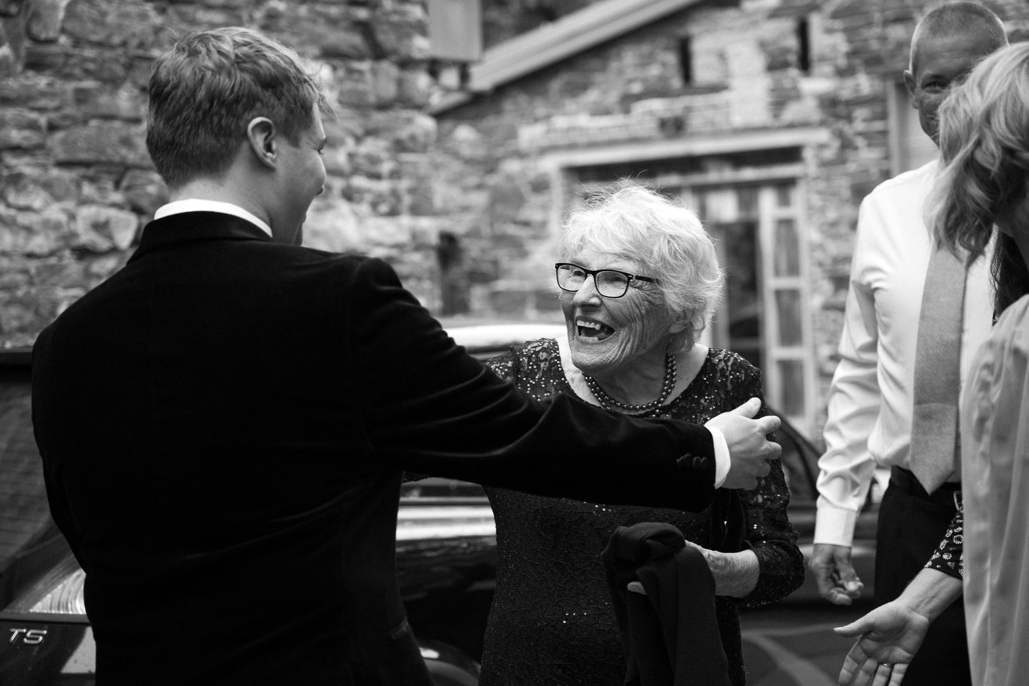 A joyful moment captured in black and white as wedding guests share embraces and laughter.
