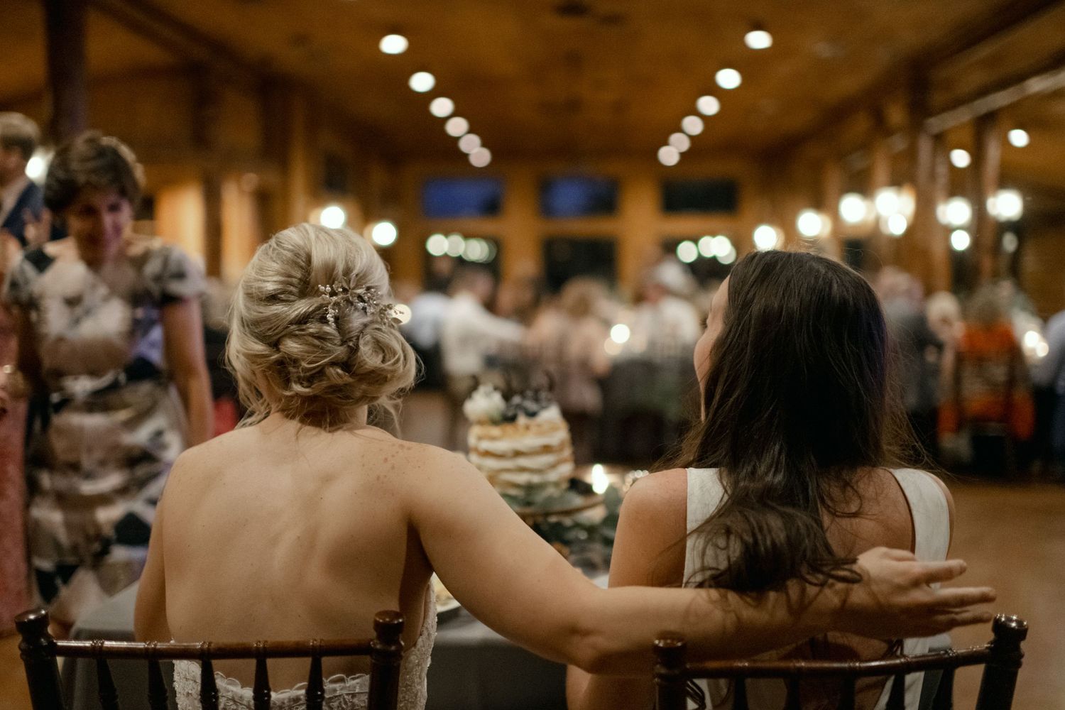 Wedding guests enjoying dinner in an elegant reception hall with warm lighting.