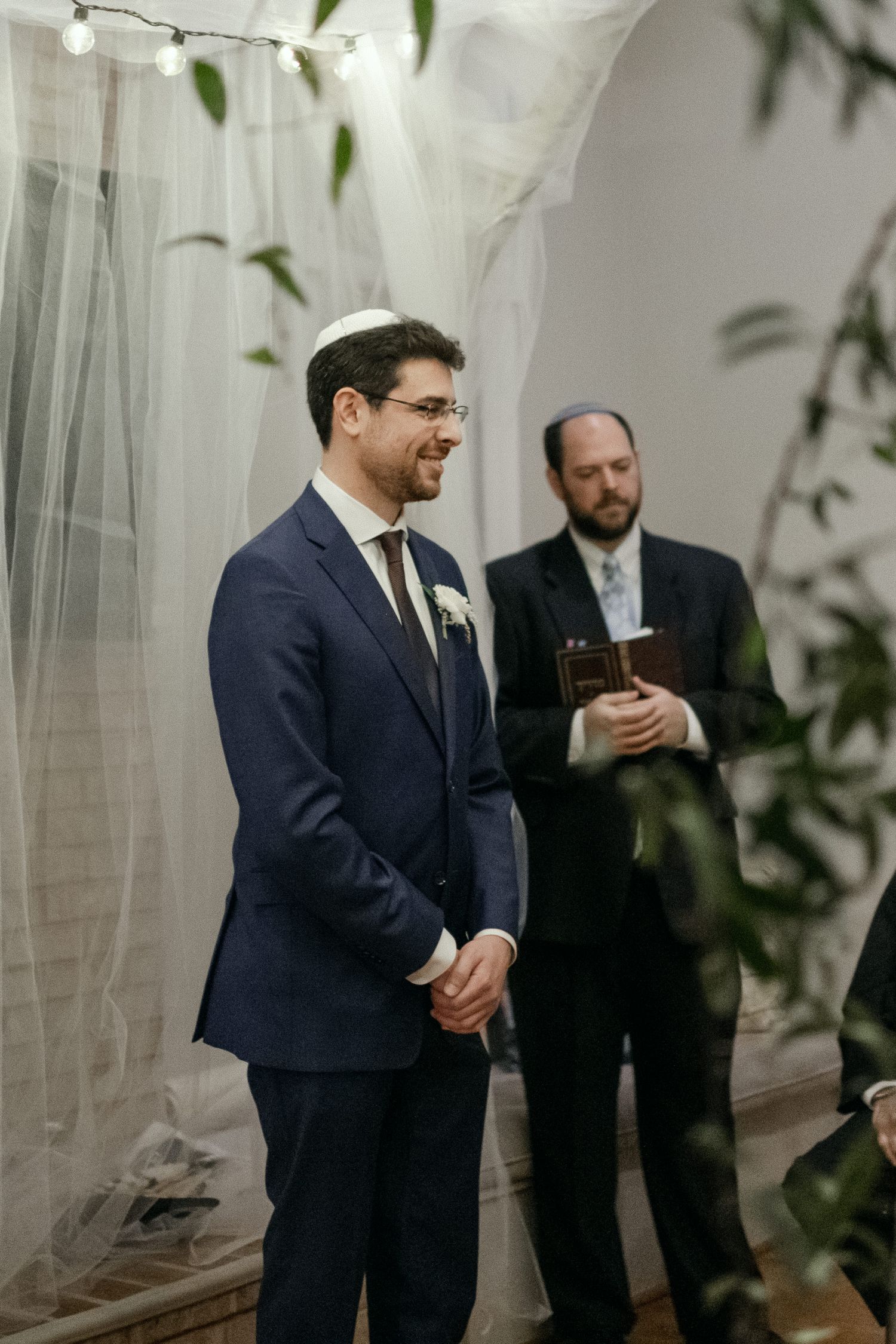 Wedding ceremony setup with sheer curtains and greenery in an indoor venue.