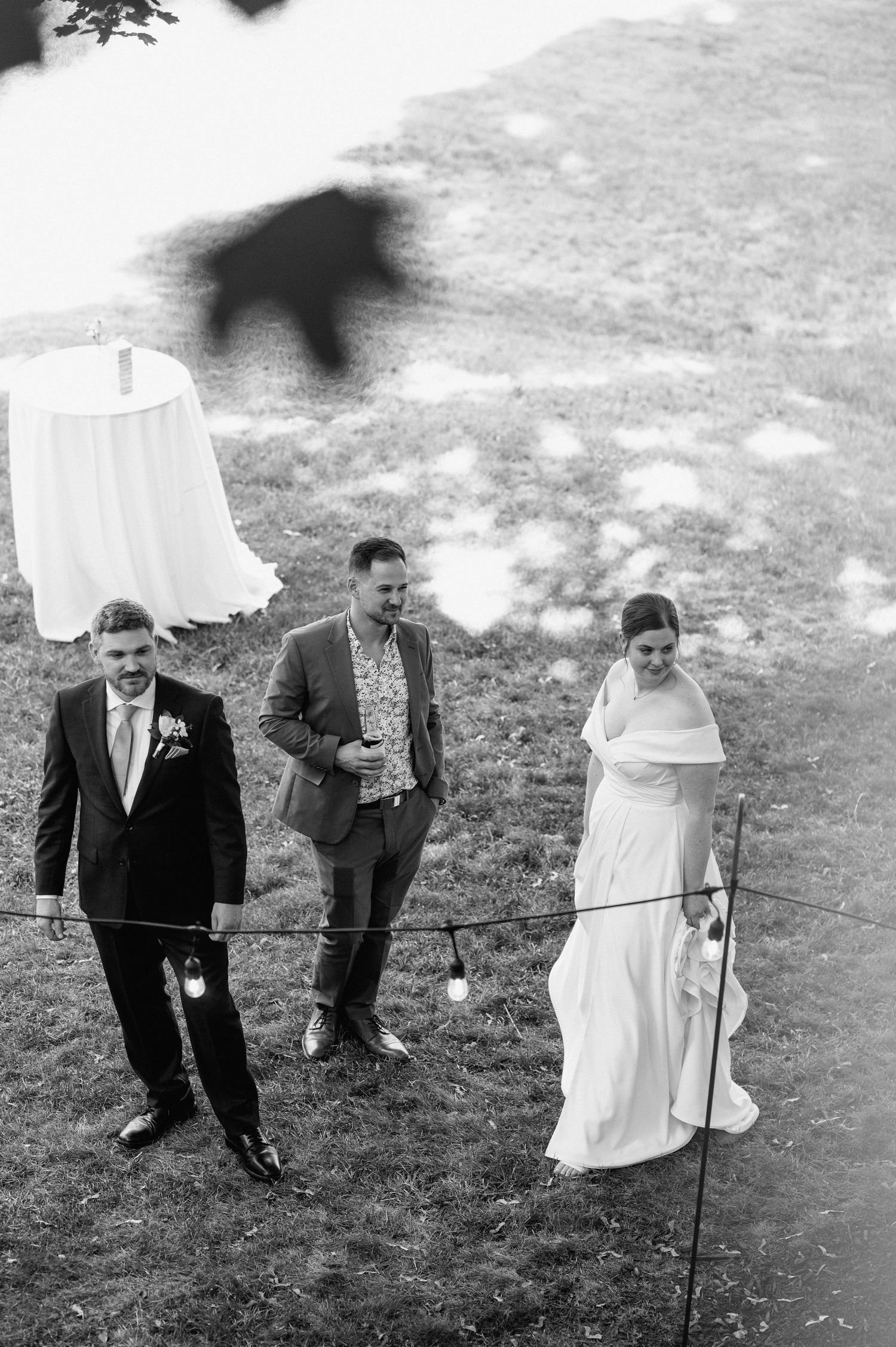 Wedding party walking down a grassy hill with a dress hanging in the background.