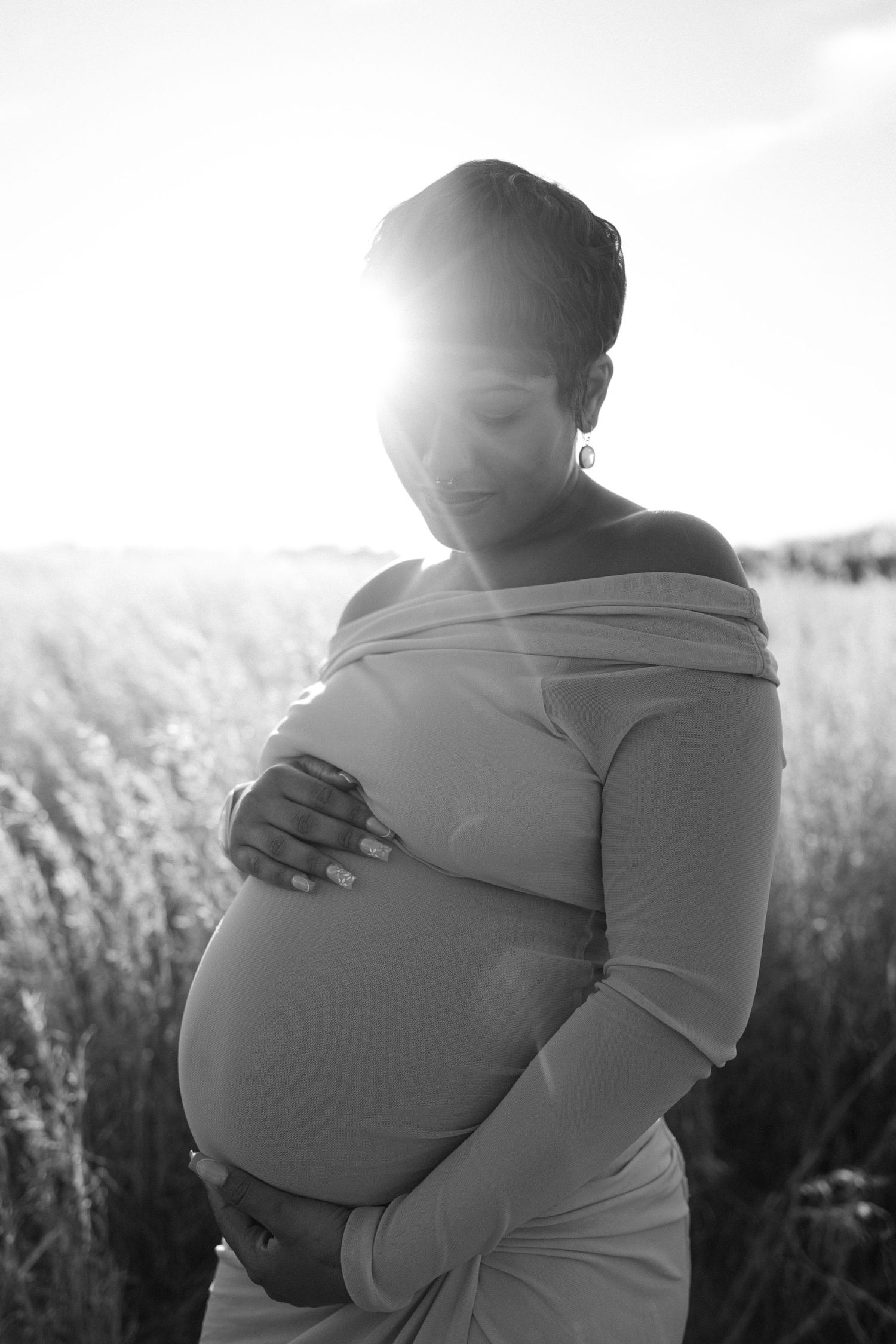 maternity photo of woman holding baby bump in field with sun glow in eldersburg