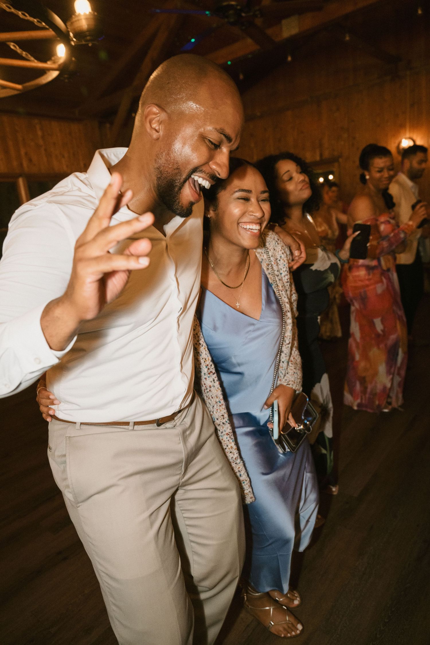 Guests dancing enthusiastically at a rustic indoor celebration with warm lighting.