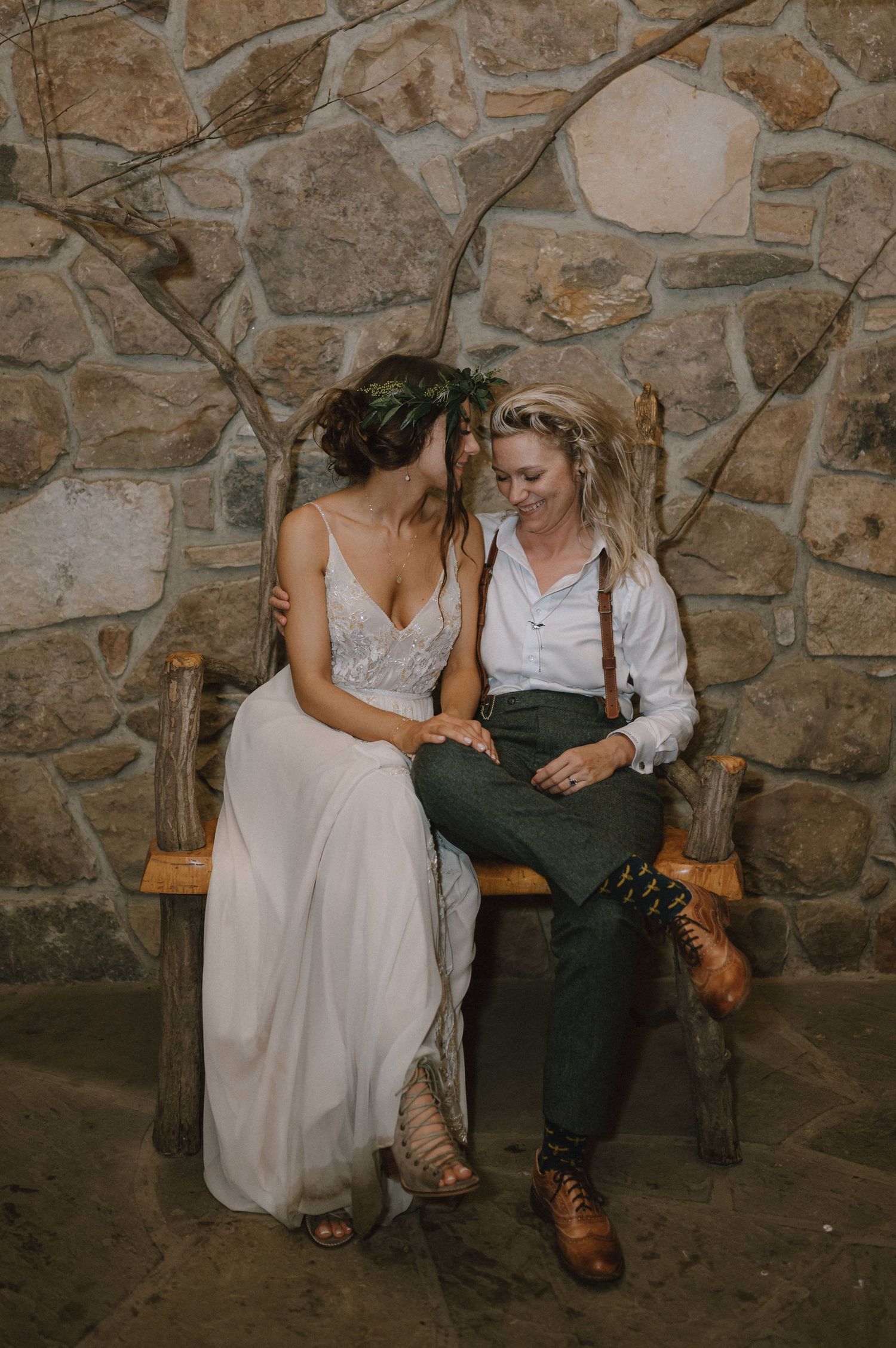 A couple shares an intimate moment while sitting on a wooden bench against a stone wall.