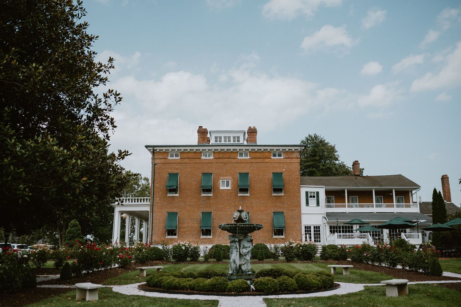 A grand brick mansion with white columns and manicured gardens on a sunny day.