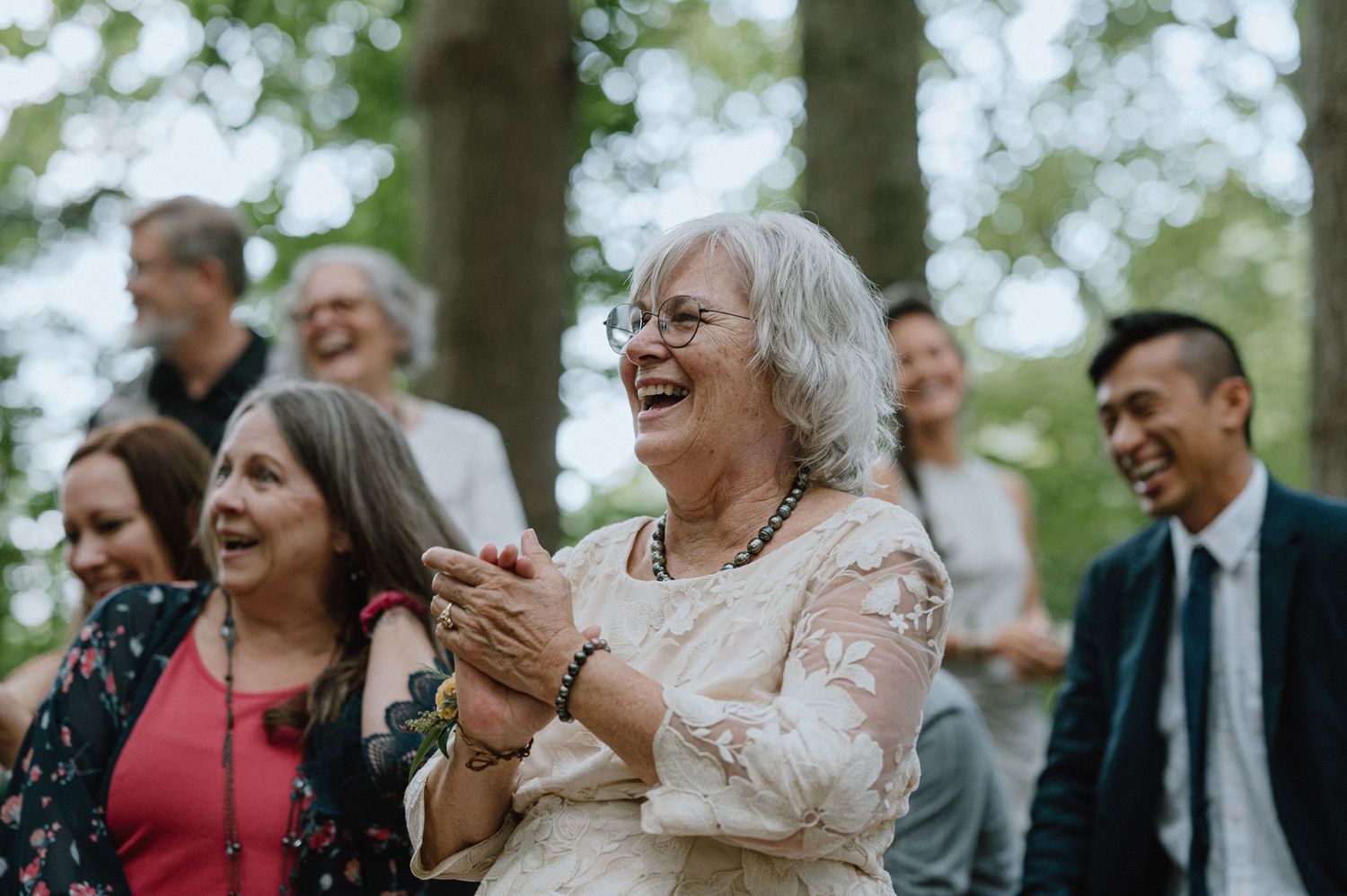Wedding guests smile and laugh during an outdoor forest celebration.