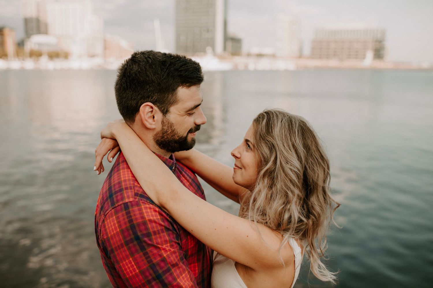 Couple in tender embrace against waterfront cityscape during golden hour.