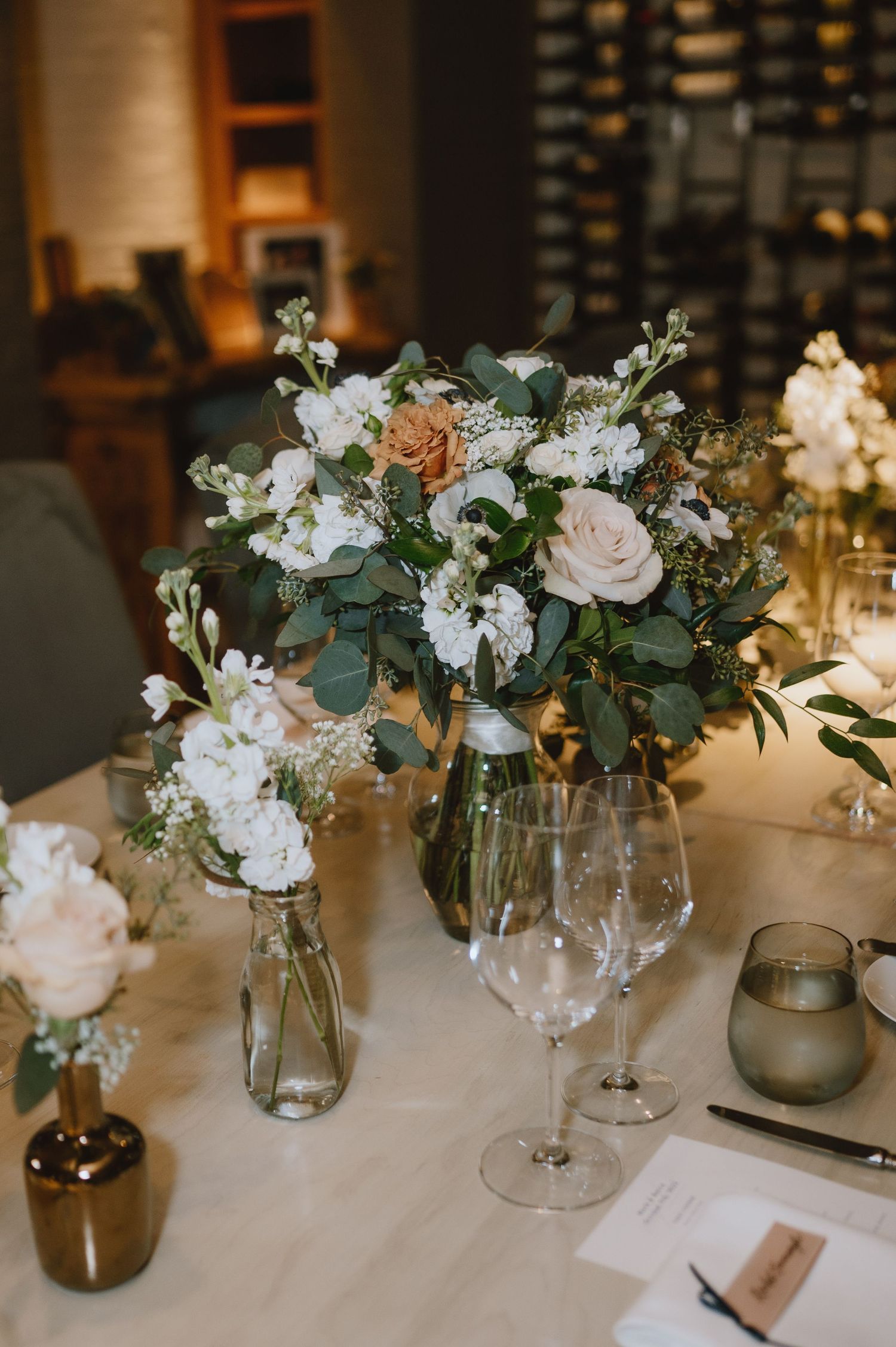 Romantic table setting with peach and white floral arrangements in glass vases.