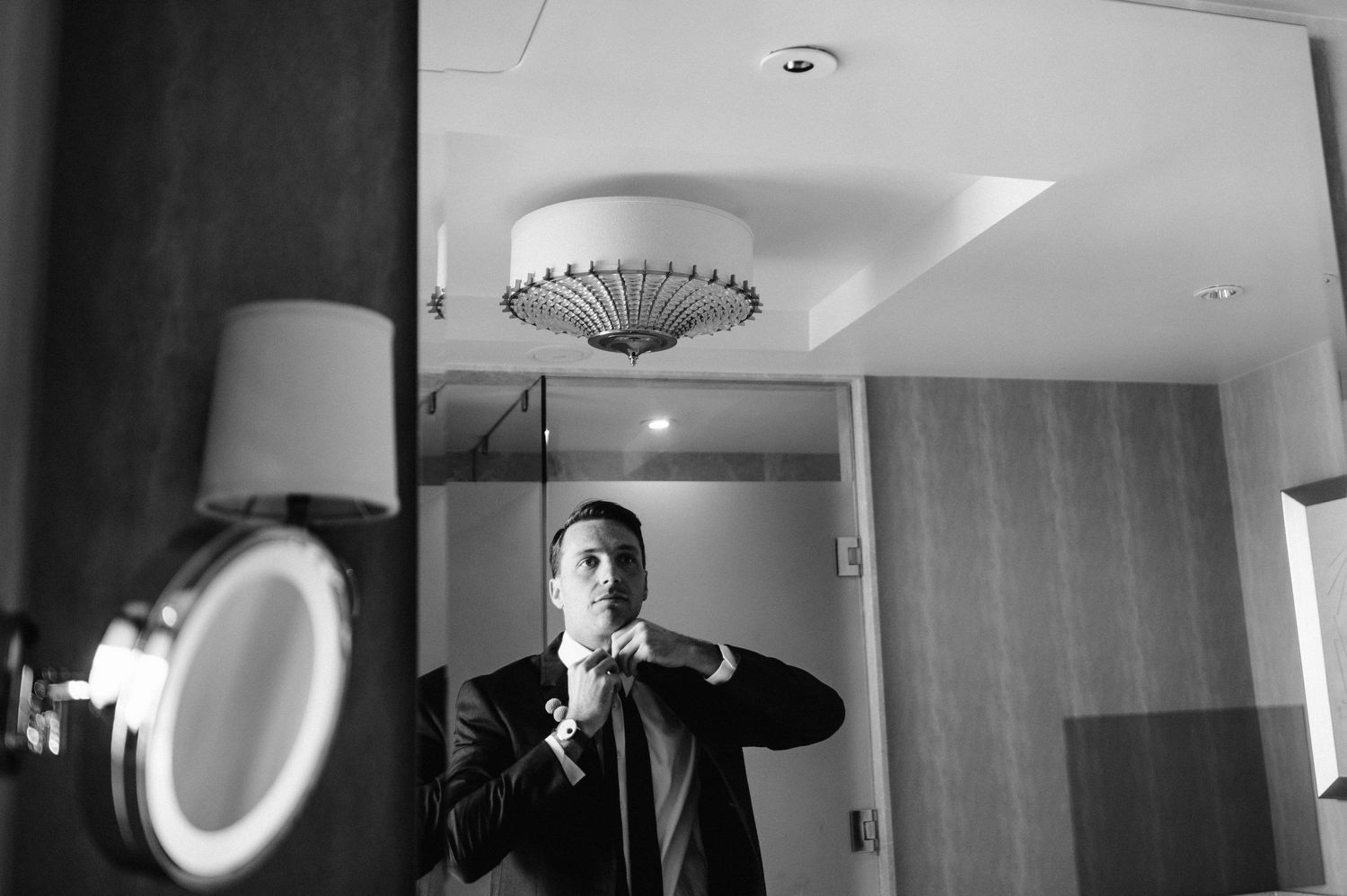 Black and white photo of formal preparation in hotel room with mirror reflection.