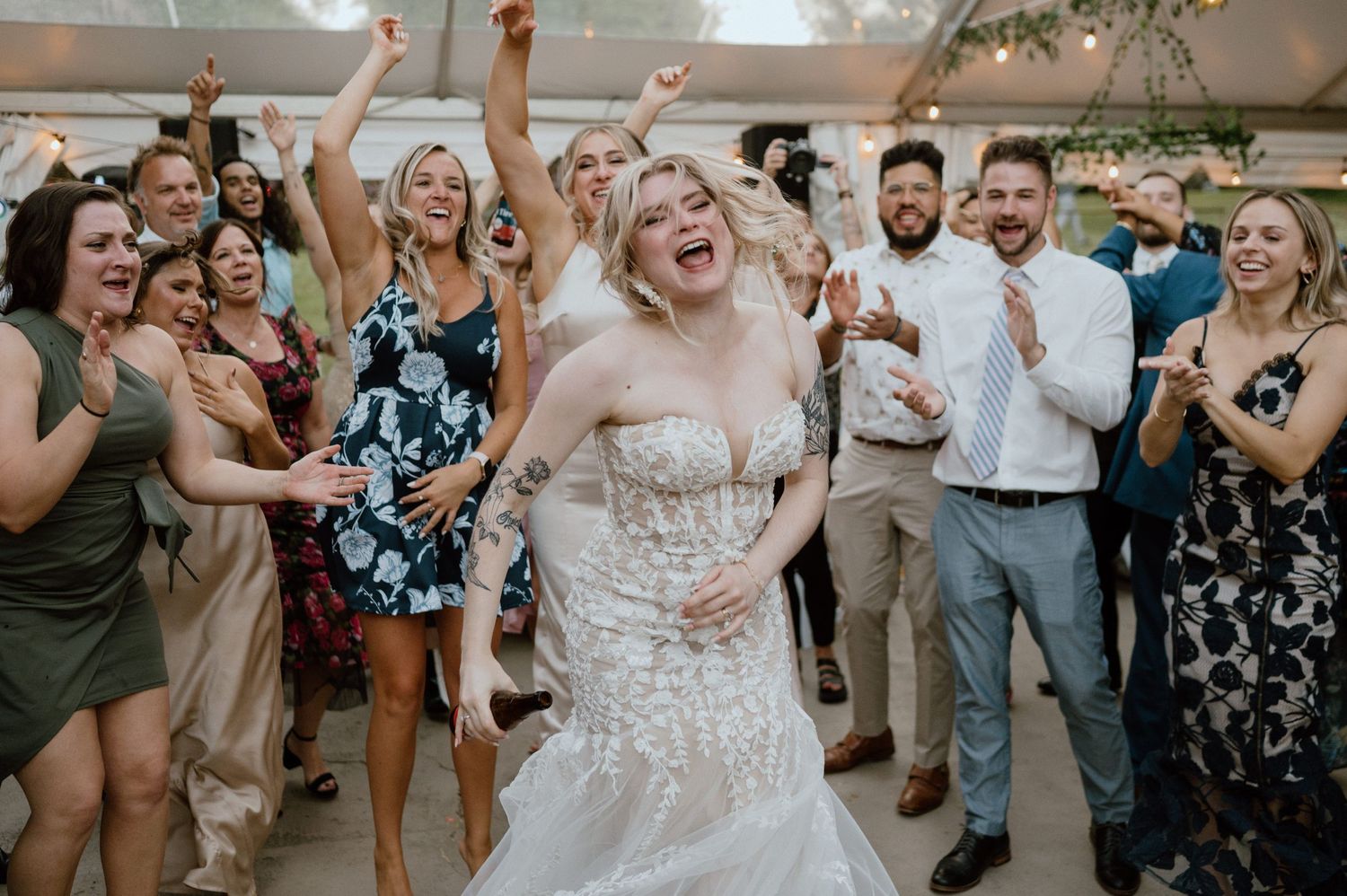 Wedding guests dancing and celebrating with joy under a white tent at an outdoor reception.