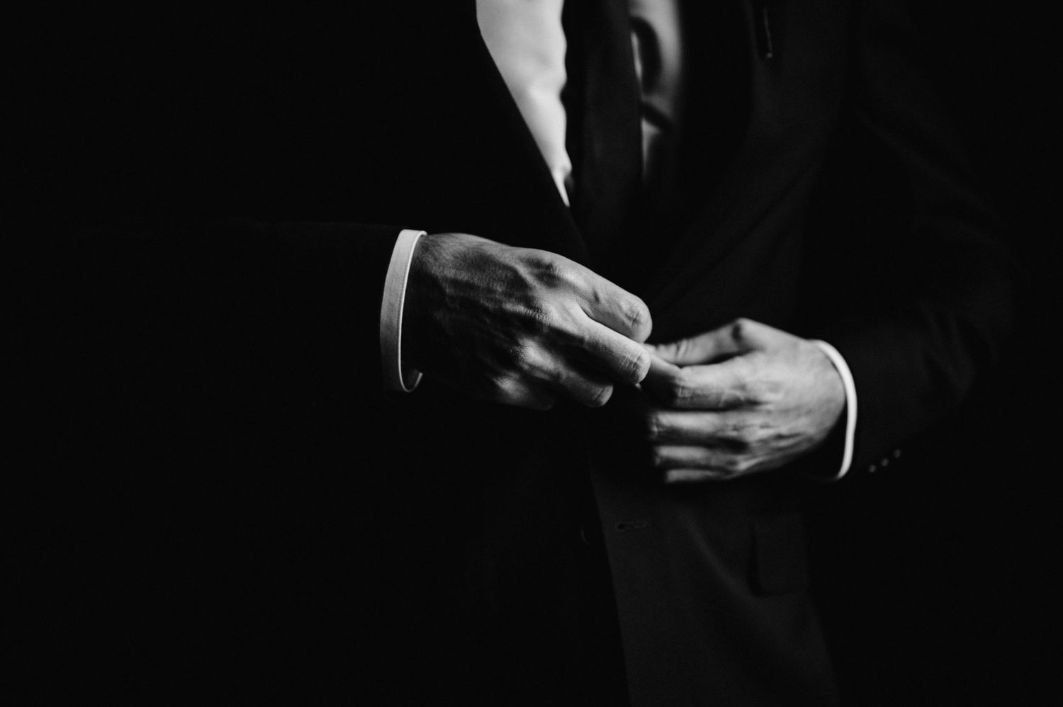 Close-up black and white photo of hands adjusting suit cuff links.
