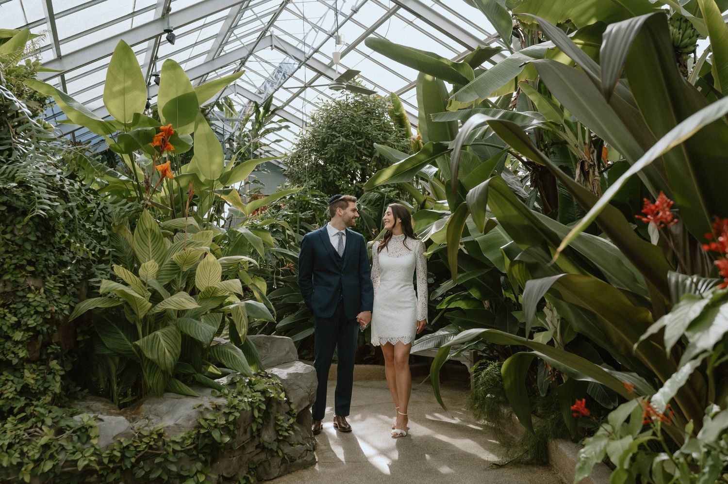 Couple walking through greenhouse filled with lush tropical plants and flowers.