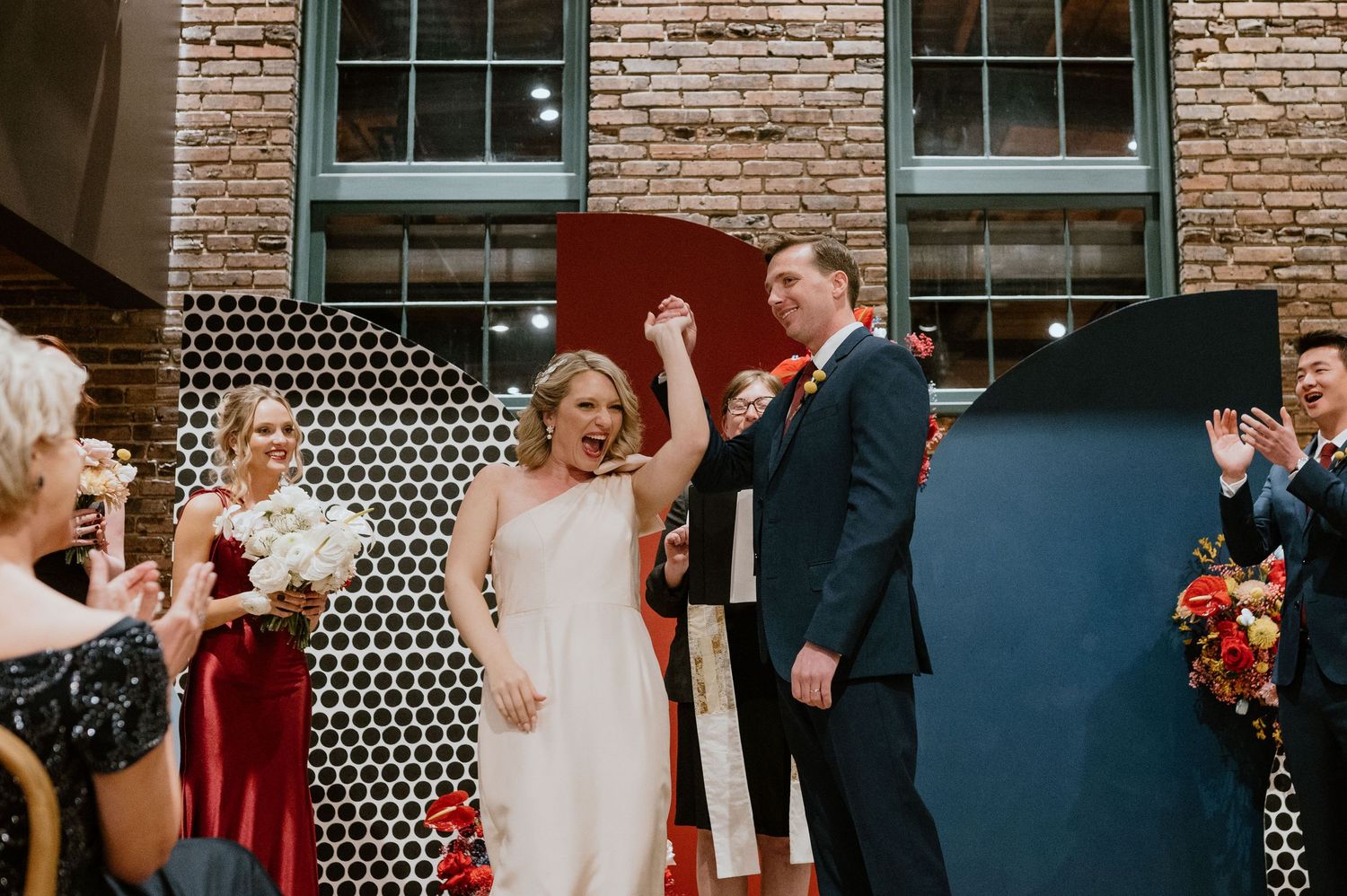 Wedding celebration with guests applauding in front of a geometric patterned backdrop.