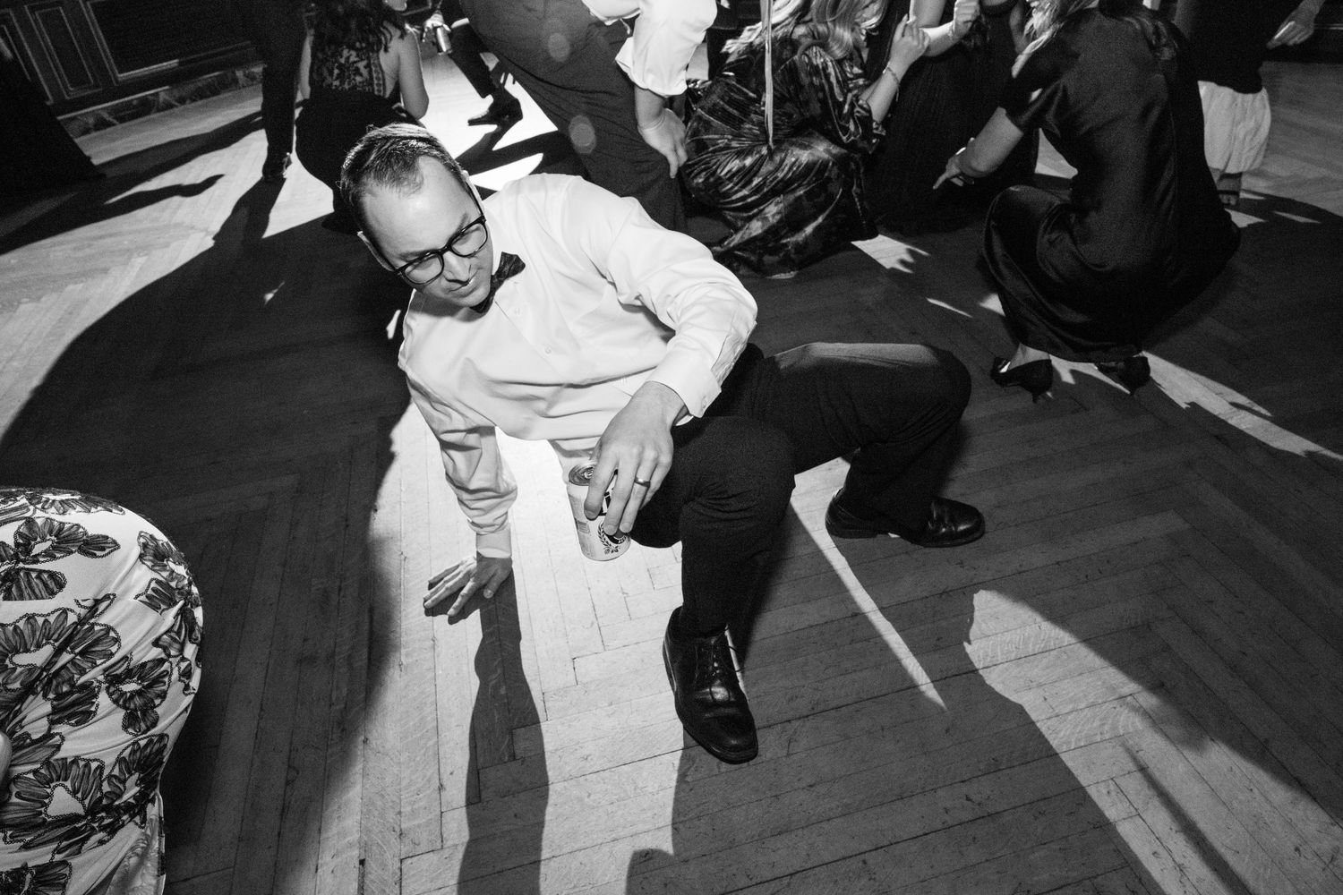 Black and white photo of wedding guests dancing energetically on a wooden dance floor.