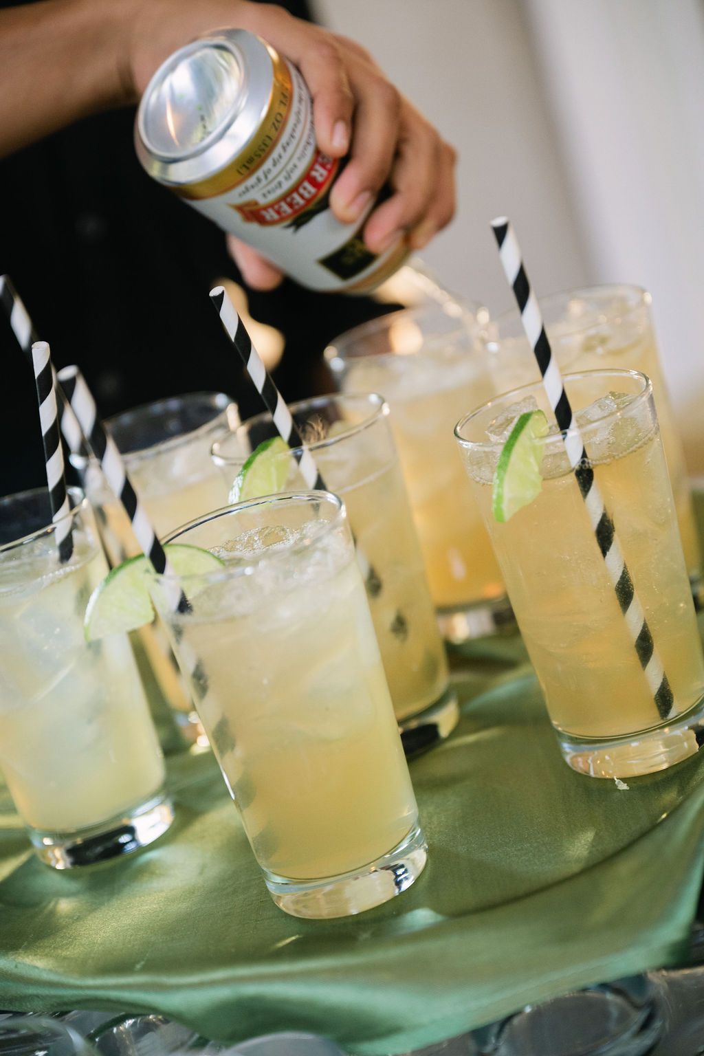 Refreshing cocktails with lime garnish and black striped straws being served on a green surface.