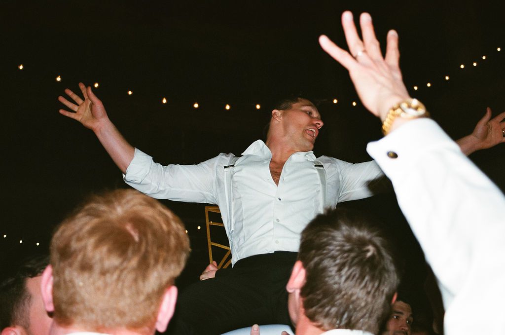 Party guests with raised hands dancing under string lights at night.