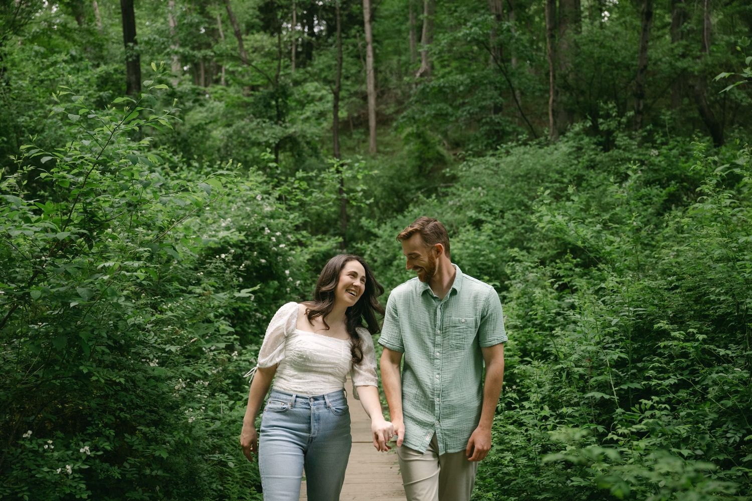 Two people walk hand in hand through a lush green forest path.