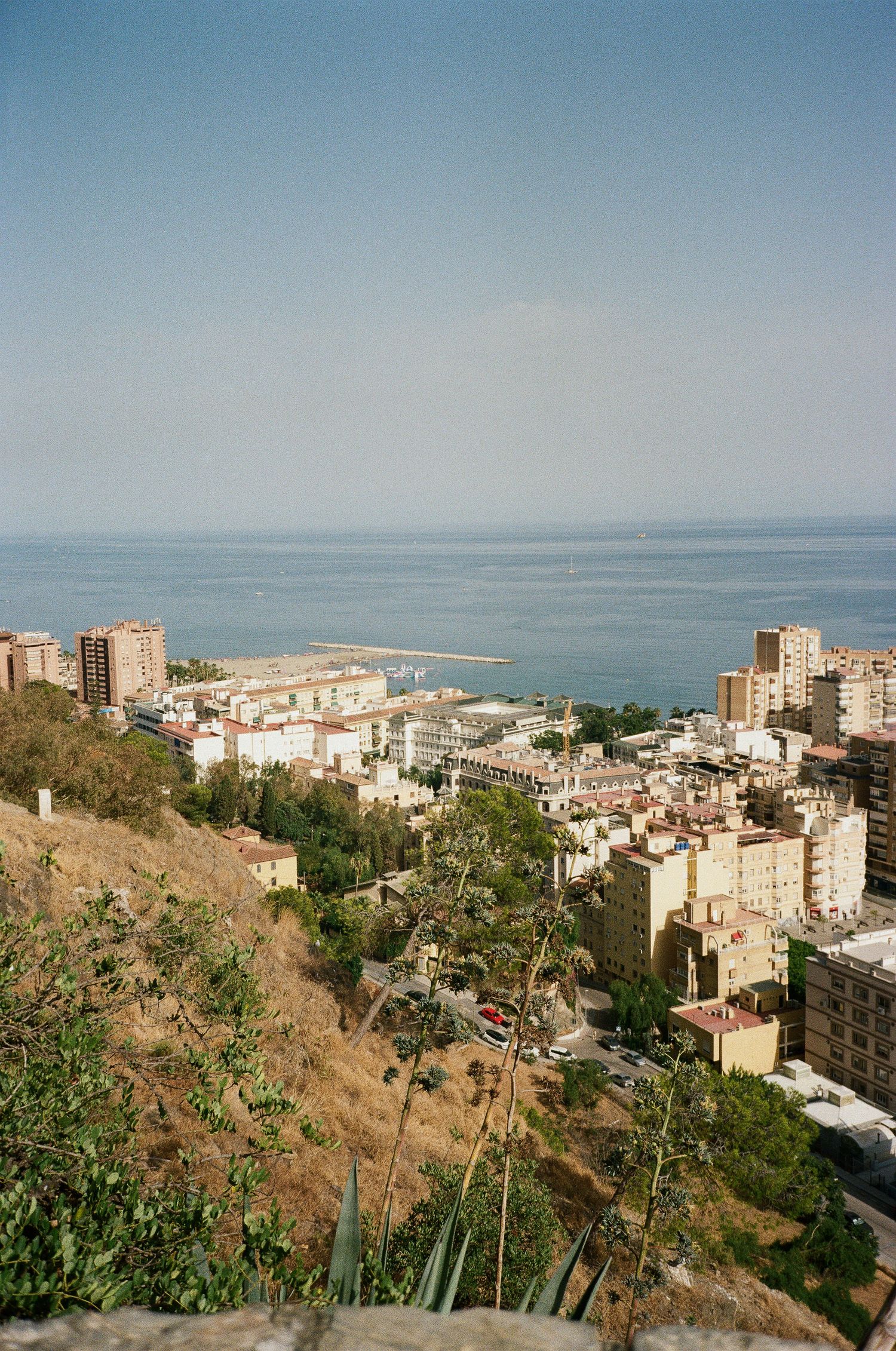 Coastal cityscape with modern buildings cascading down hillside towards Mediterranean Sea.