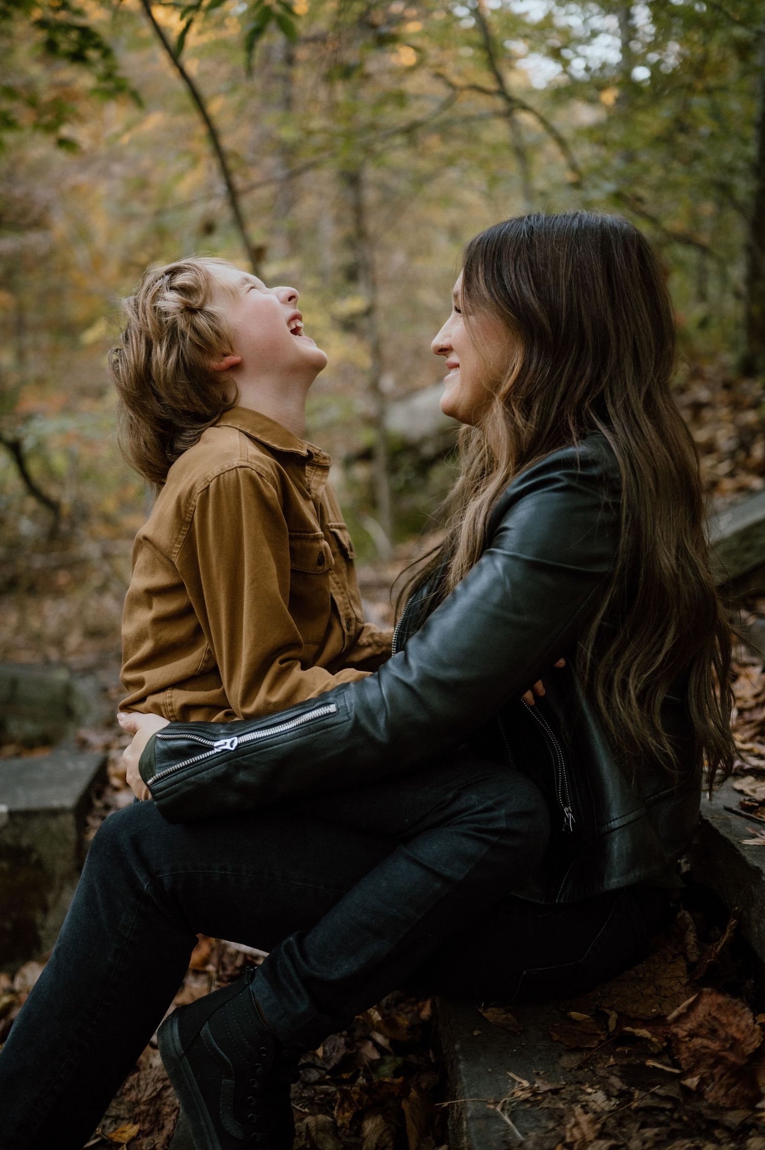 Two people share infectious laughter while sitting on wooden steps in a forest.