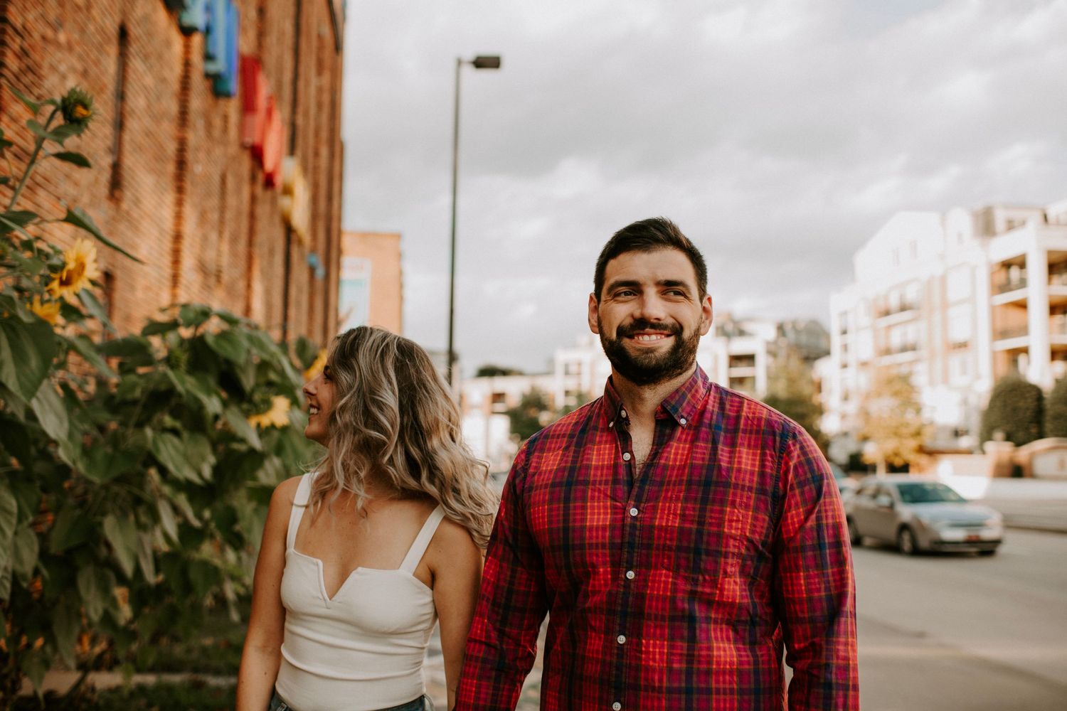 Couple walking along urban street with brick buildings in background.
