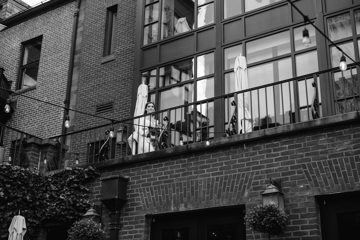 Black and white architectural photo of a brick building with balcony and string lights.