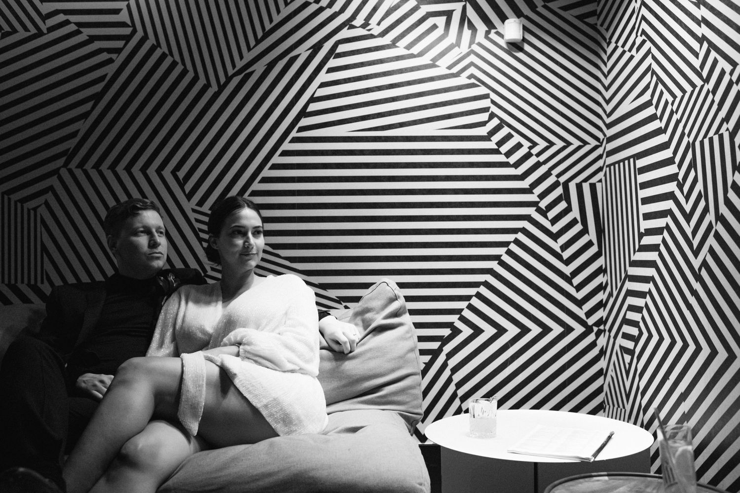 Couple sitting against geometric black and white patterned wall in artistic setting.