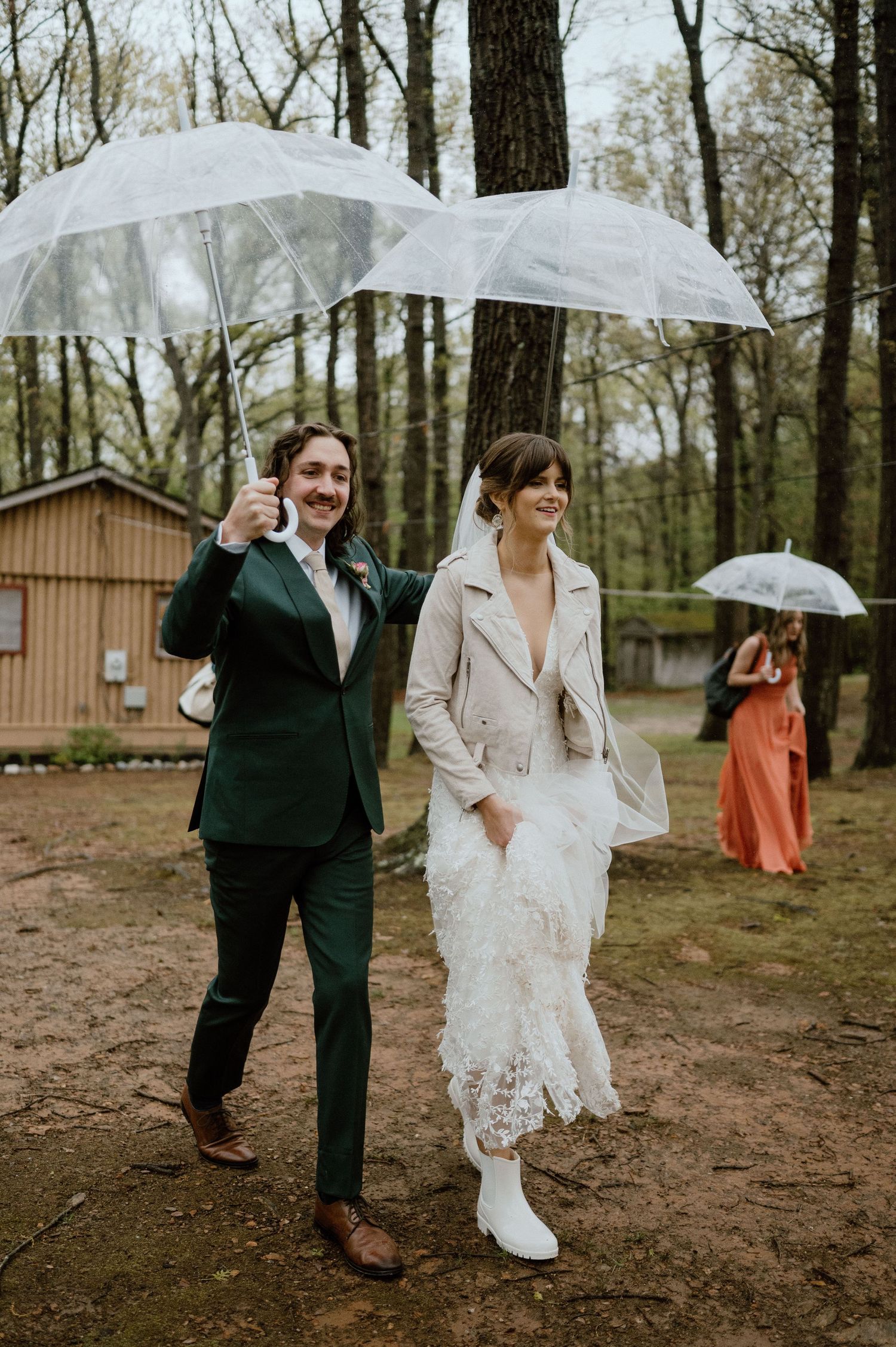 Wedding couple walking with clear umbrellas in a rainy forest setting.