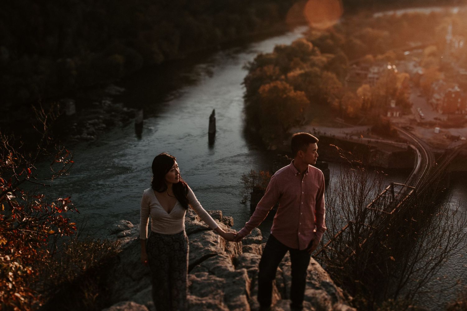 Two people walk hand in hand along a scenic path beside a tranquil lake at sunset.