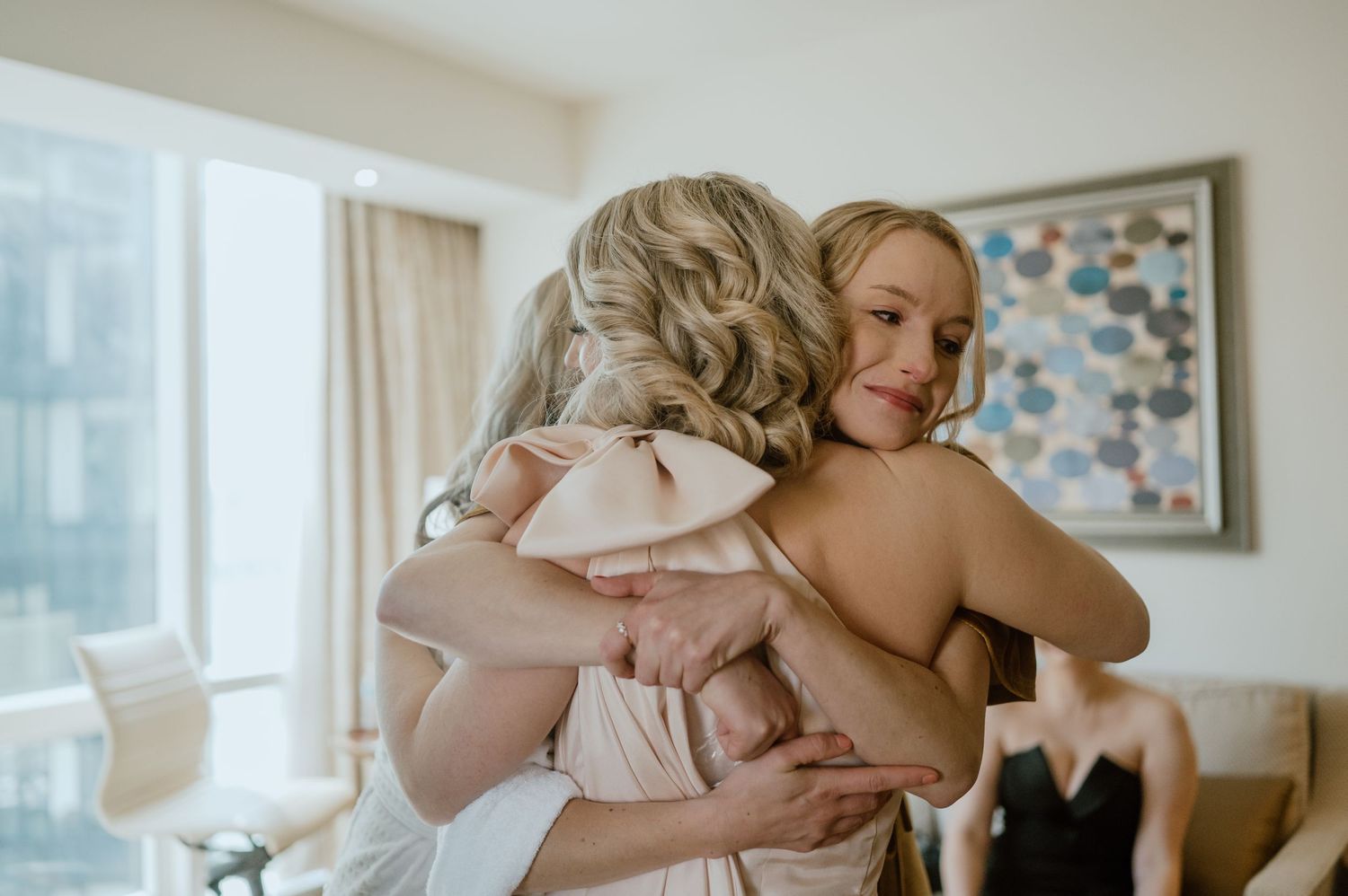 Emotional embrace captured during wedding morning preparations in bright hotel room.