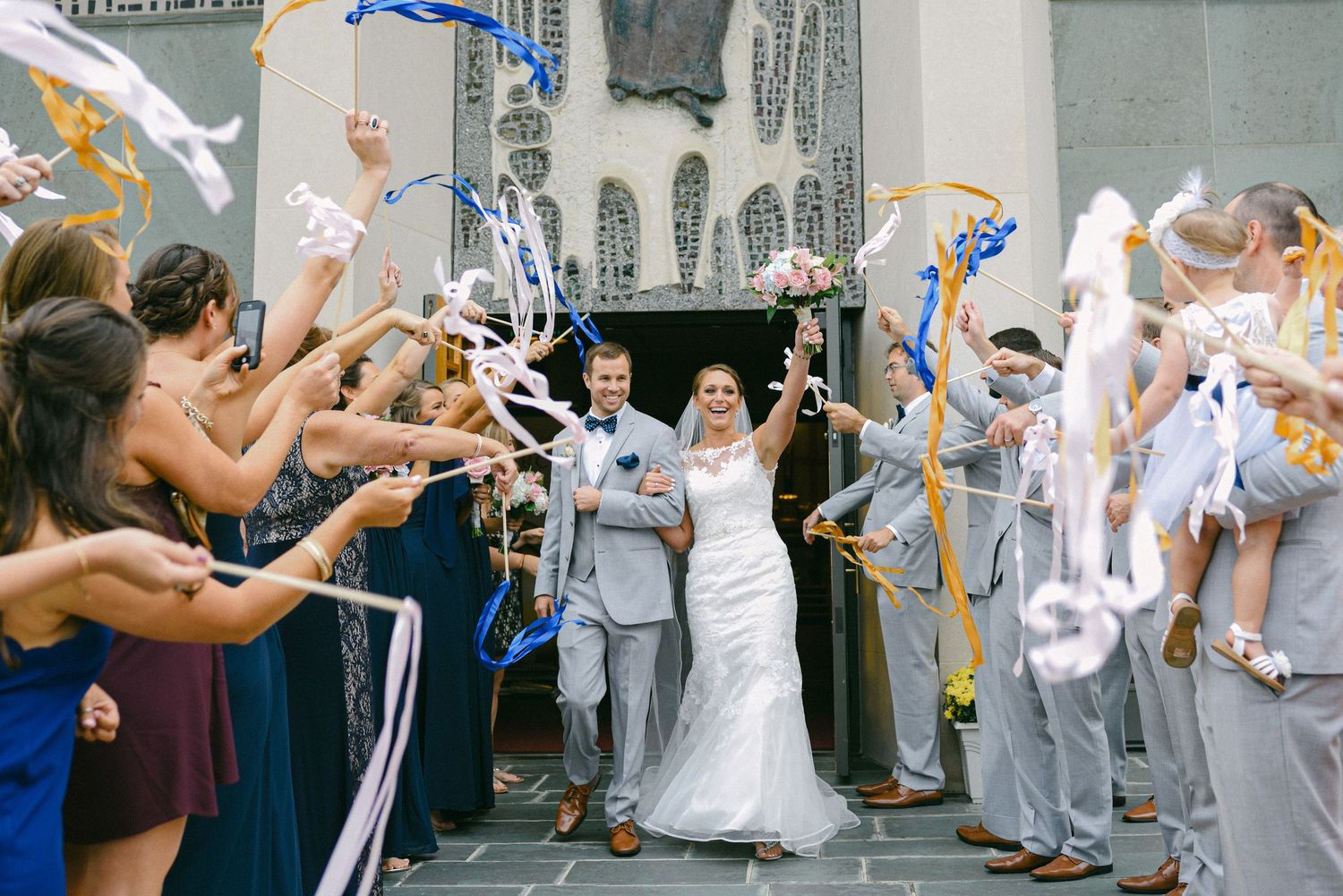 Wedding exit celebration with guests throwing blue streamers as couple descends church steps.