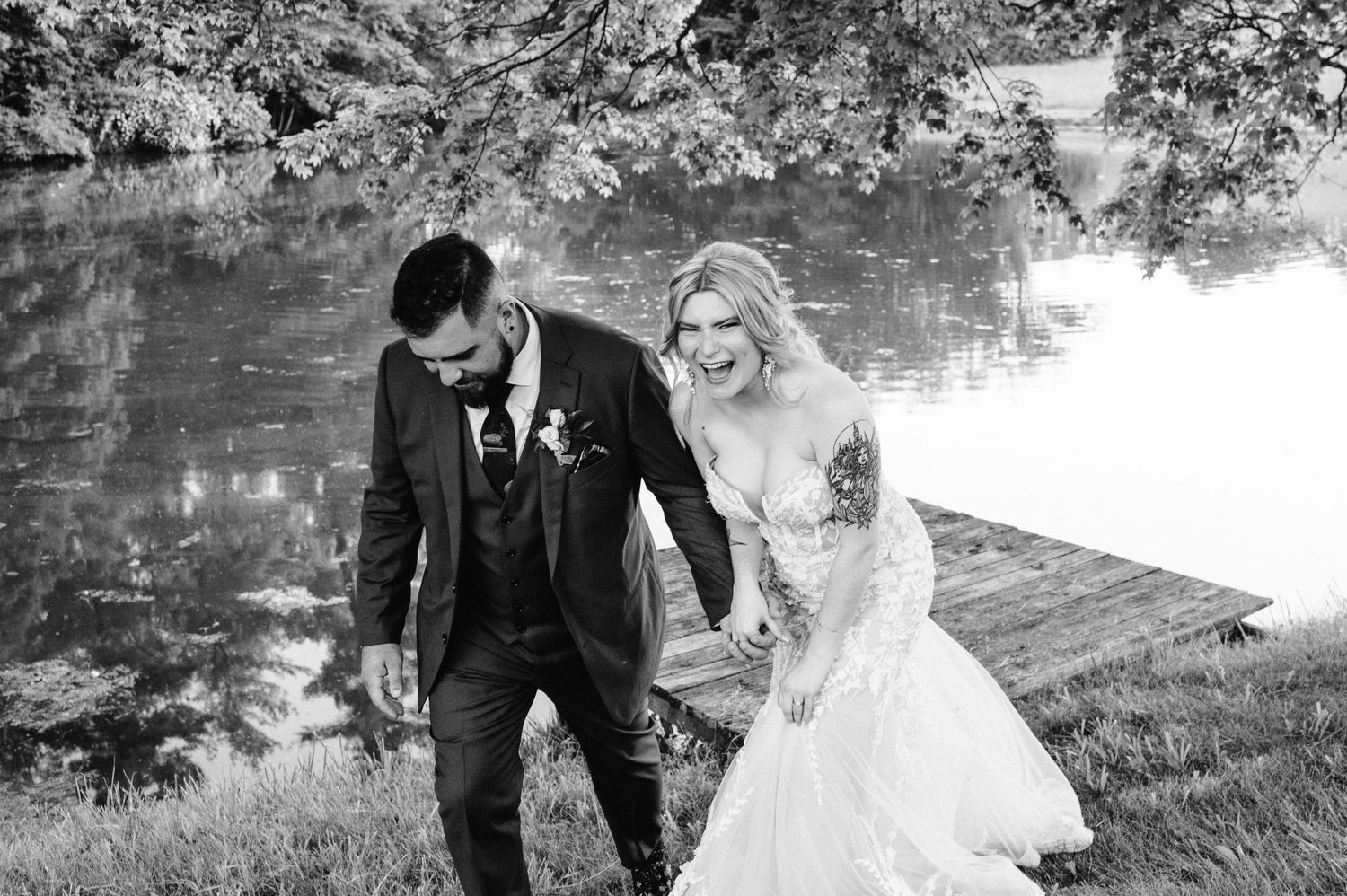 Black and white portrait of newlyweds sharing a laugh by peaceful pond.