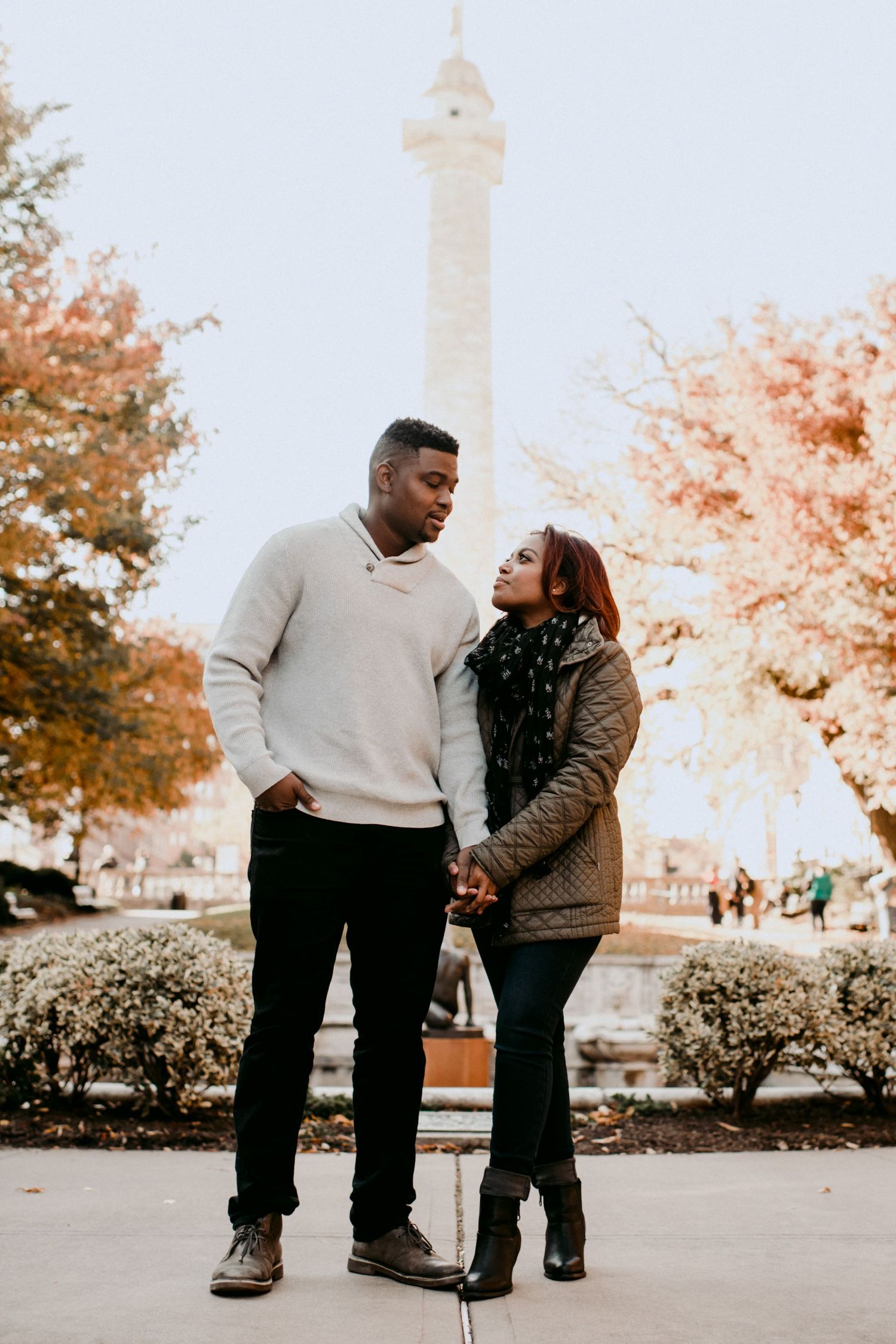A romantic couple pose in front of a tall monument during fall.