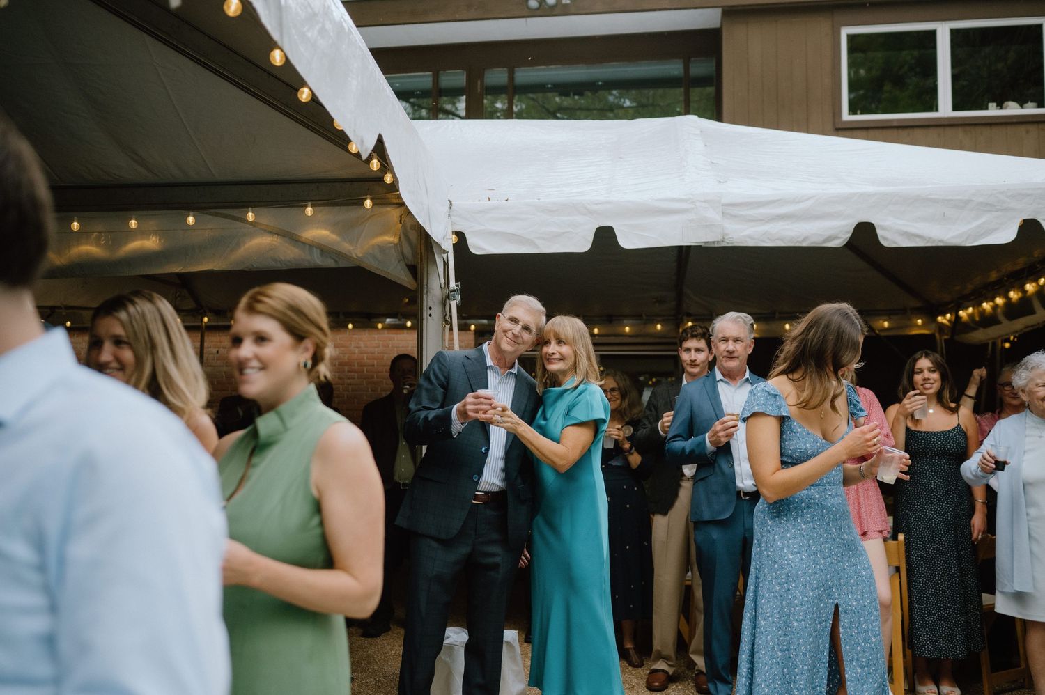 Guests mingling and socializing at an outdoor event under string lights.