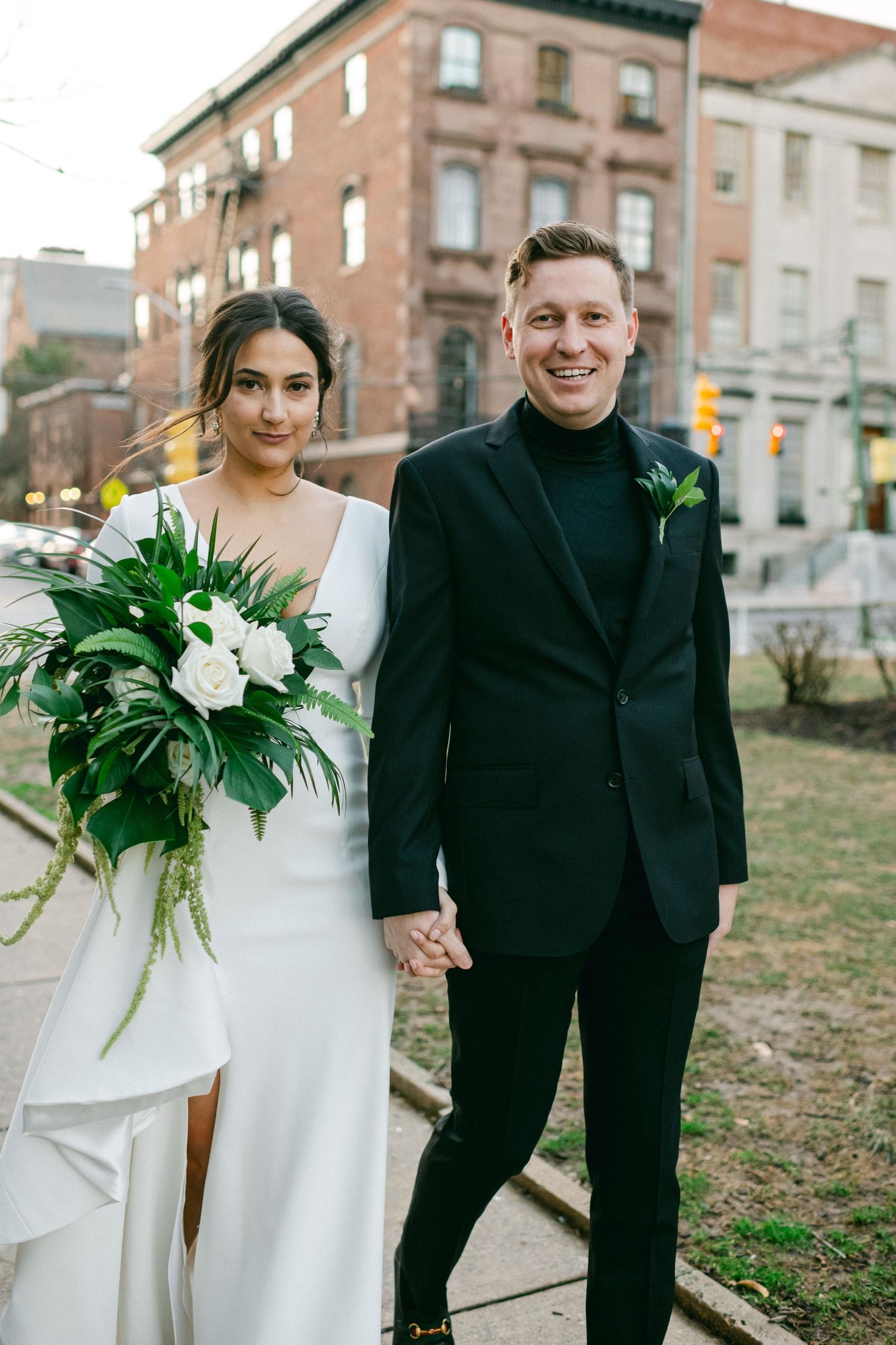 A wedding couple poses on an urban sidewalk with brick buildings in the background.