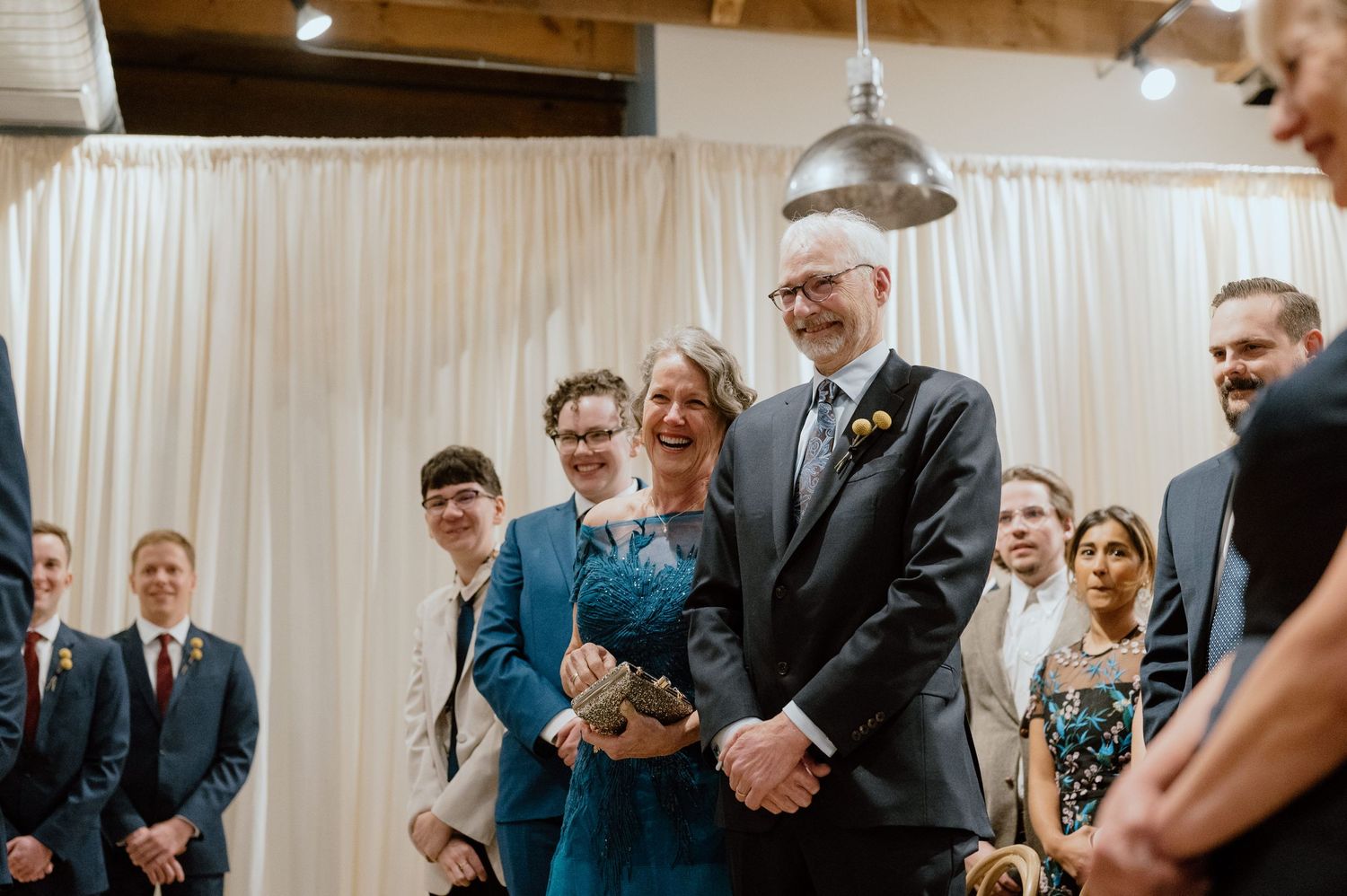 Wedding ceremony guests gathered in an indoor venue with industrial lighting.