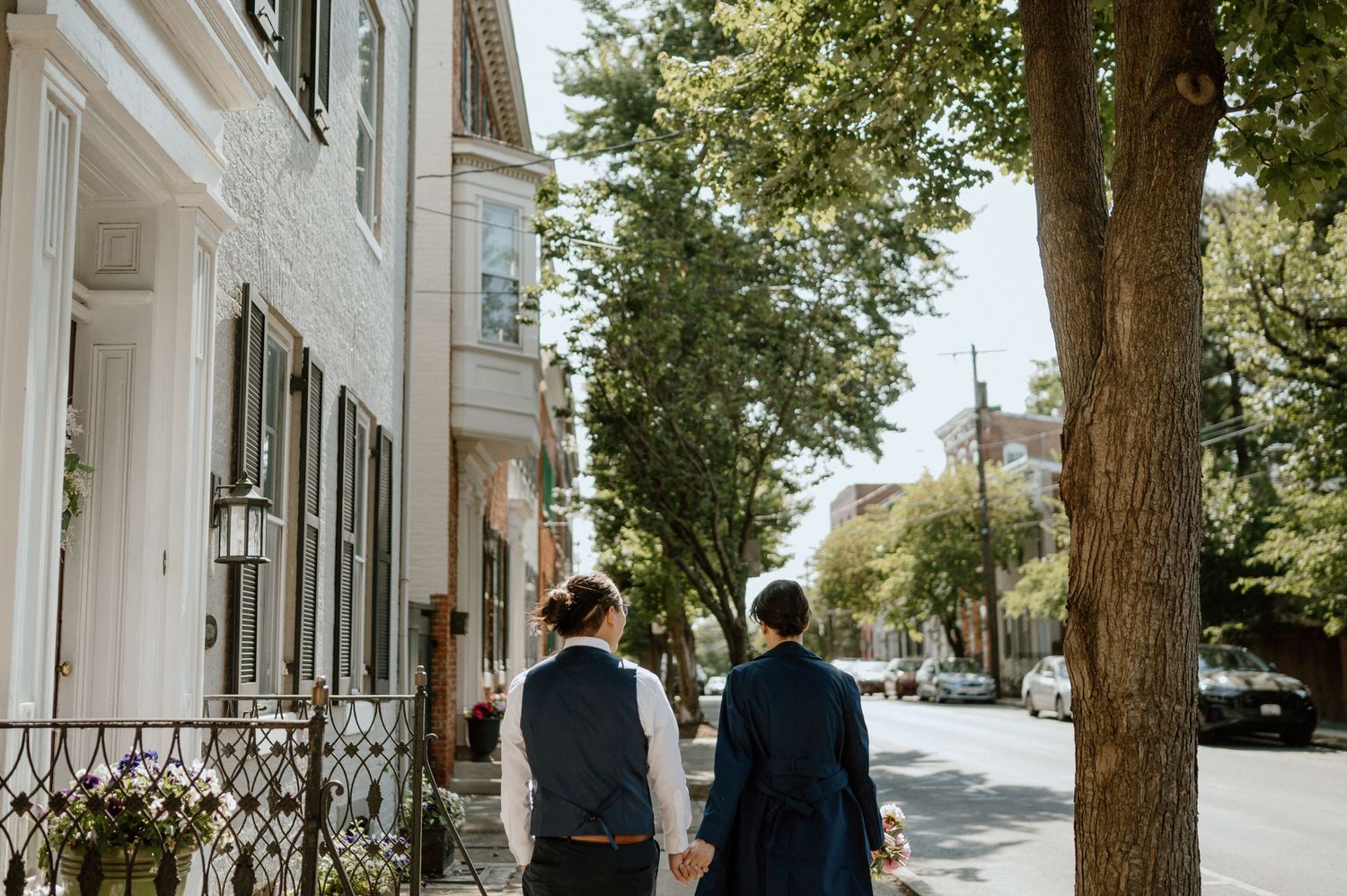 A couple walks down a tree-lined historic street wearing matching navy outfits.