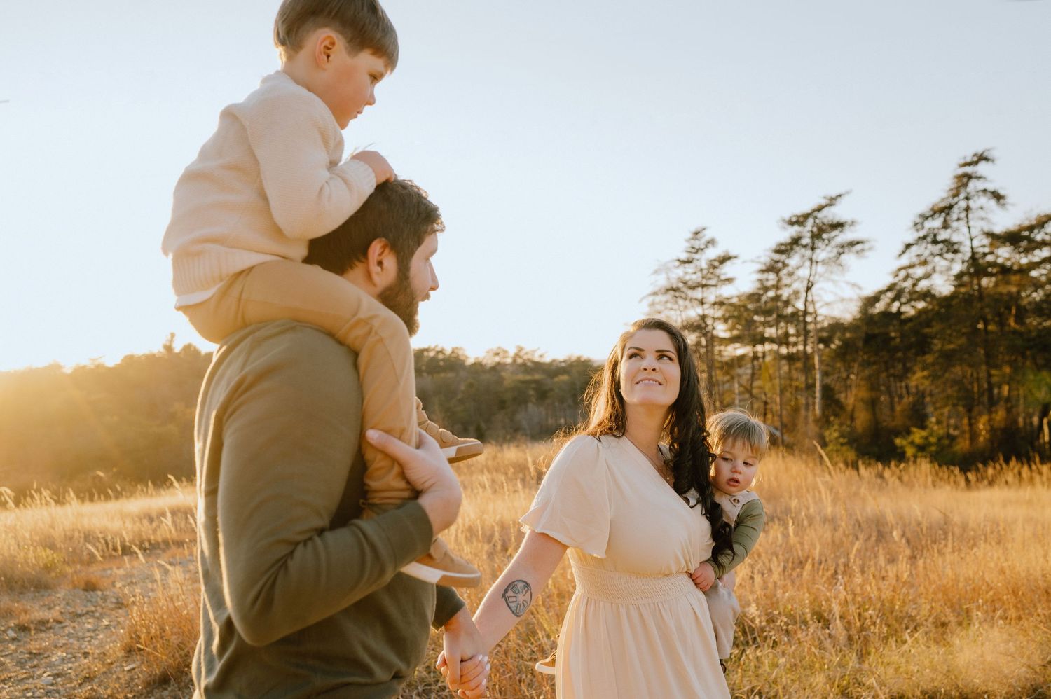 A family enjoys a sunset moment together in a golden field with tall pine trees in the background.