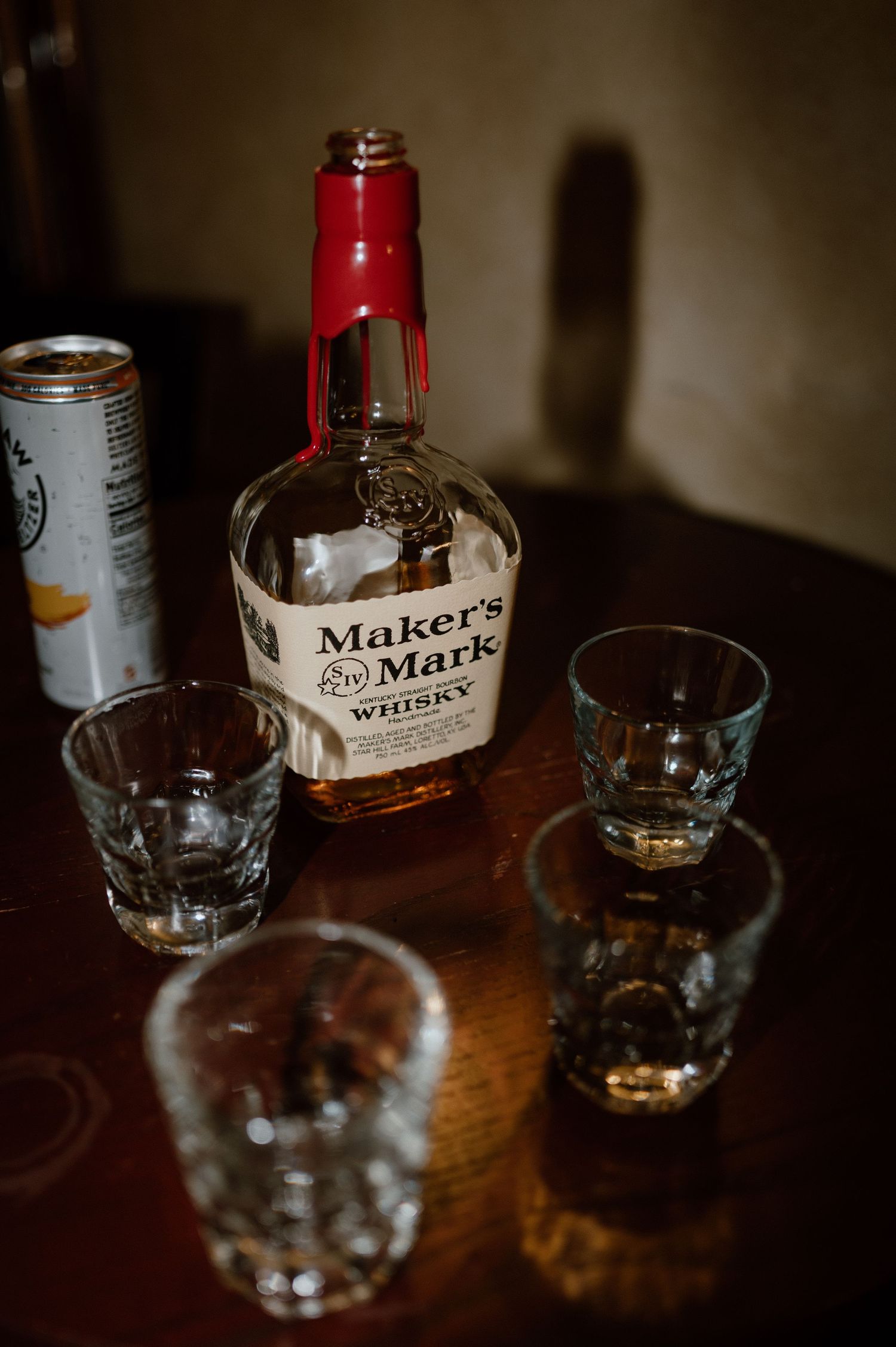 A bottle of Maker's Mark whiskey with empty glasses on a dark wooden table.
