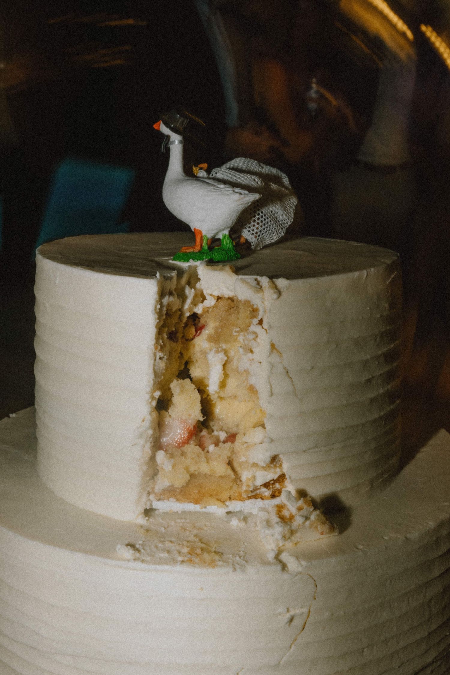 Close-up of a white wedding cake with a decorative goose topper and exposed layers showing the interior texture.