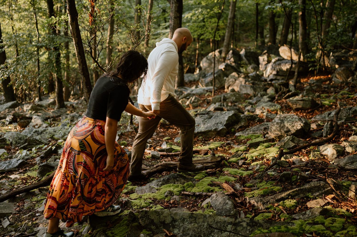 Couple climbing rocky terrain together in autumn forest setting.