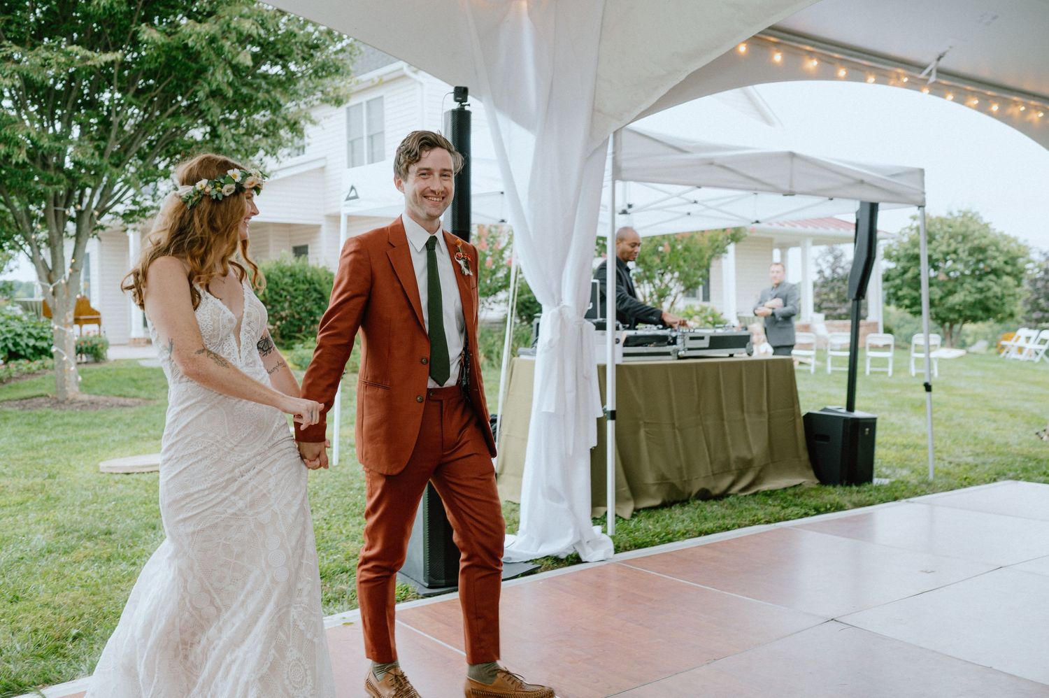 A couple entering their wedding reception tent, with white draping and string lights visible.