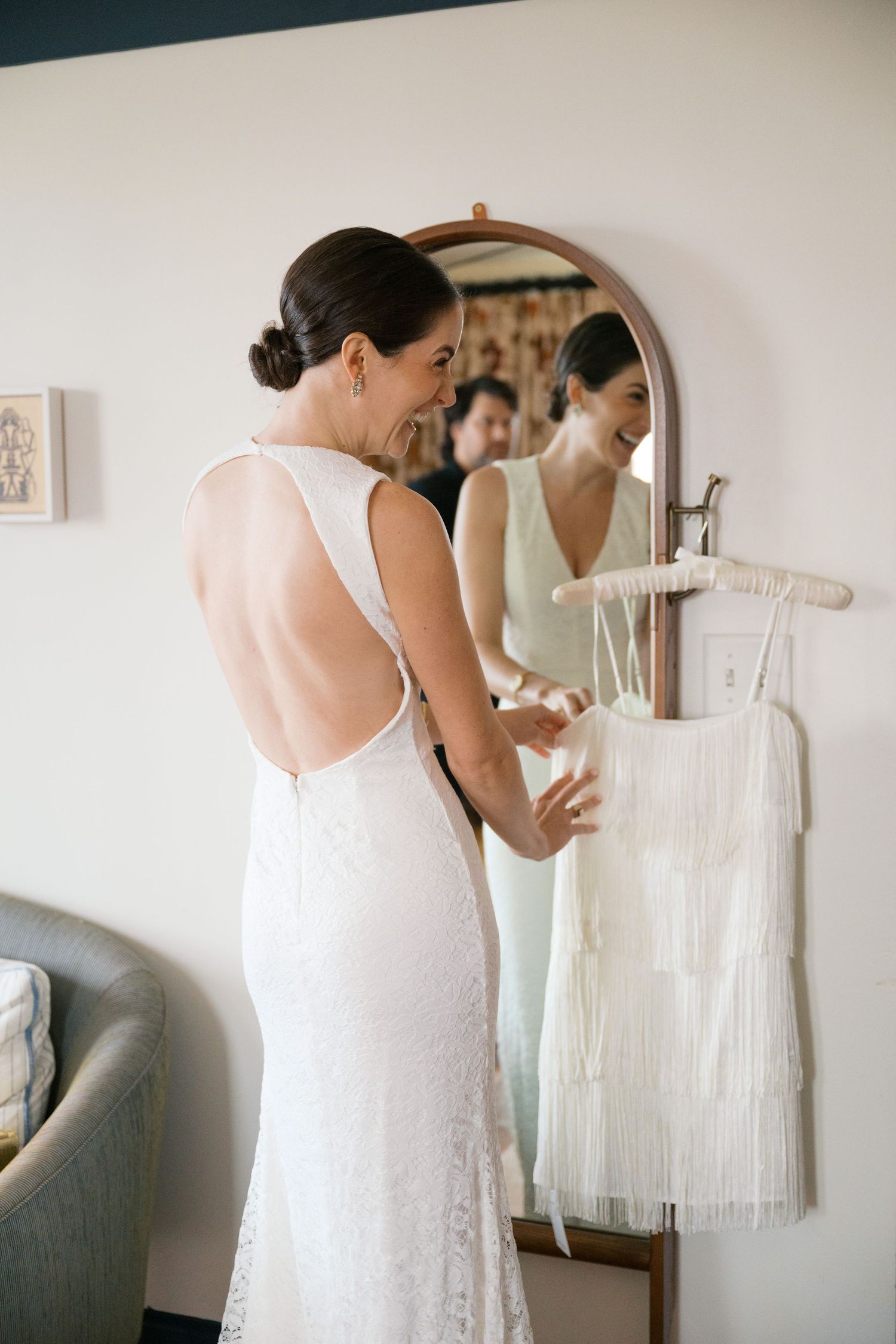 Elegant backless wedding dress being fitted in a room with a large mirror.